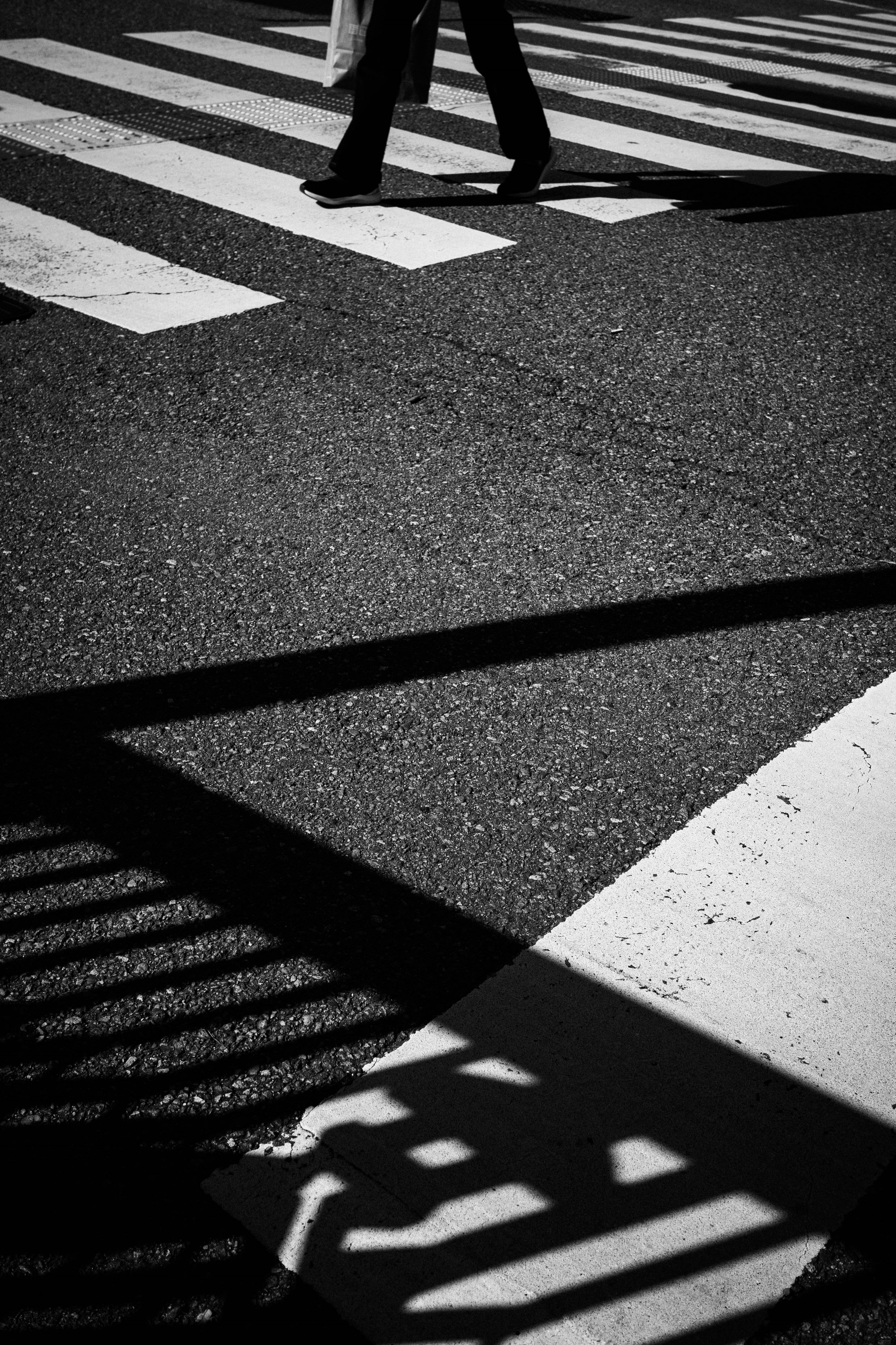 Silhouette di una persona che cammina su un attraversamento pedonale in bianco e nero con forte contrasto di ombre