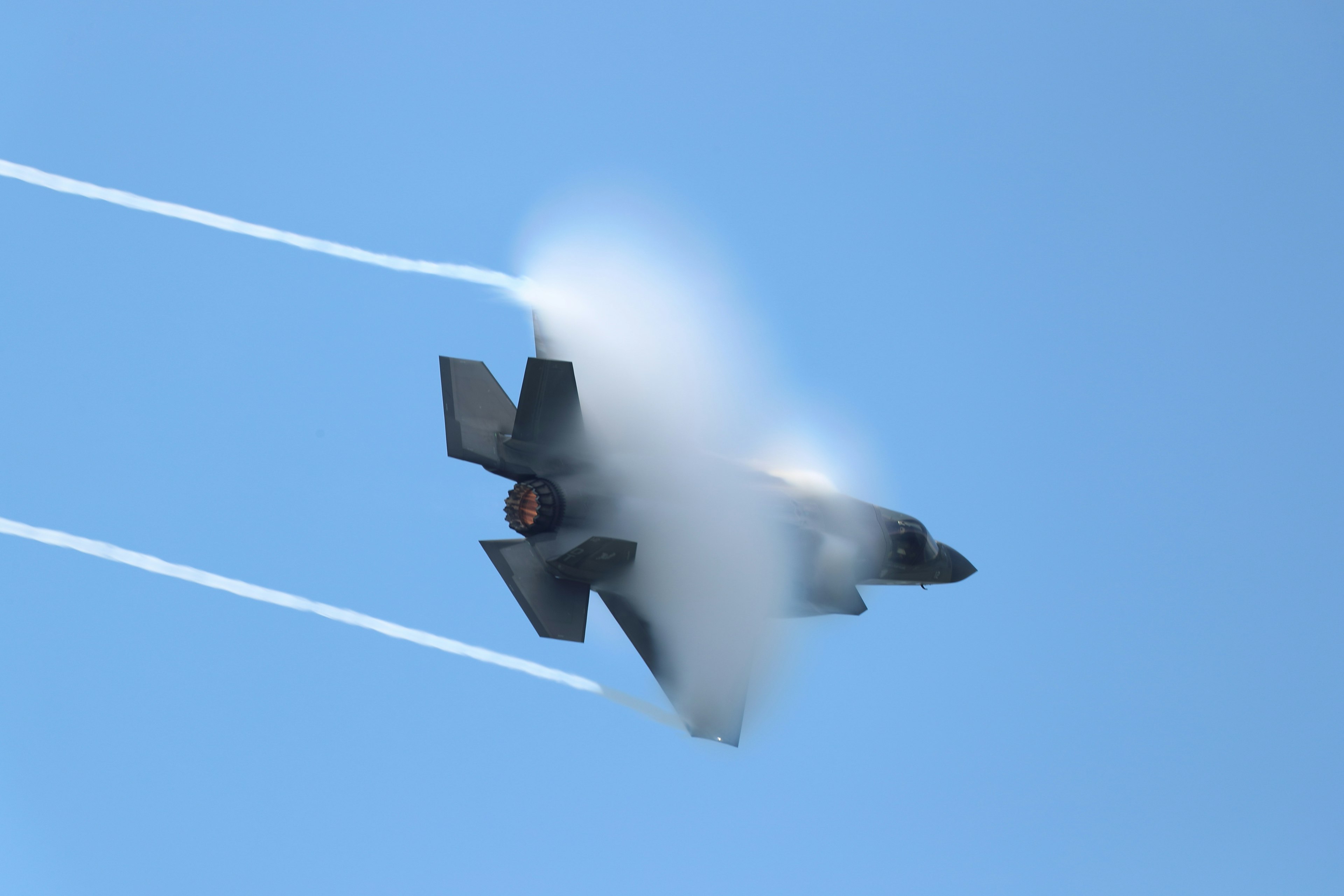 F-35 fighter jet flying with vapor trails against a blue sky