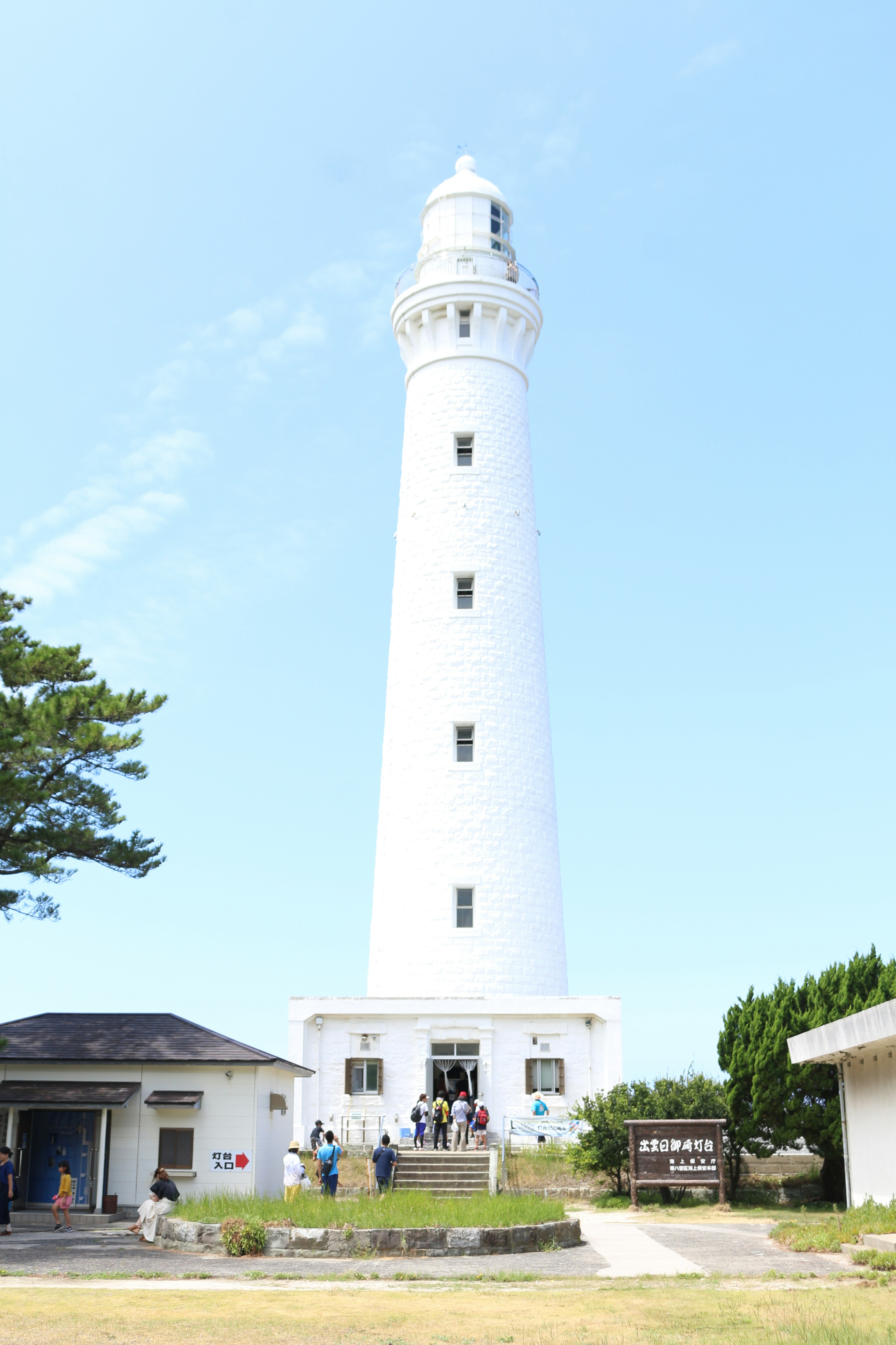 White lighthouse against a blue sky with visitors nearby