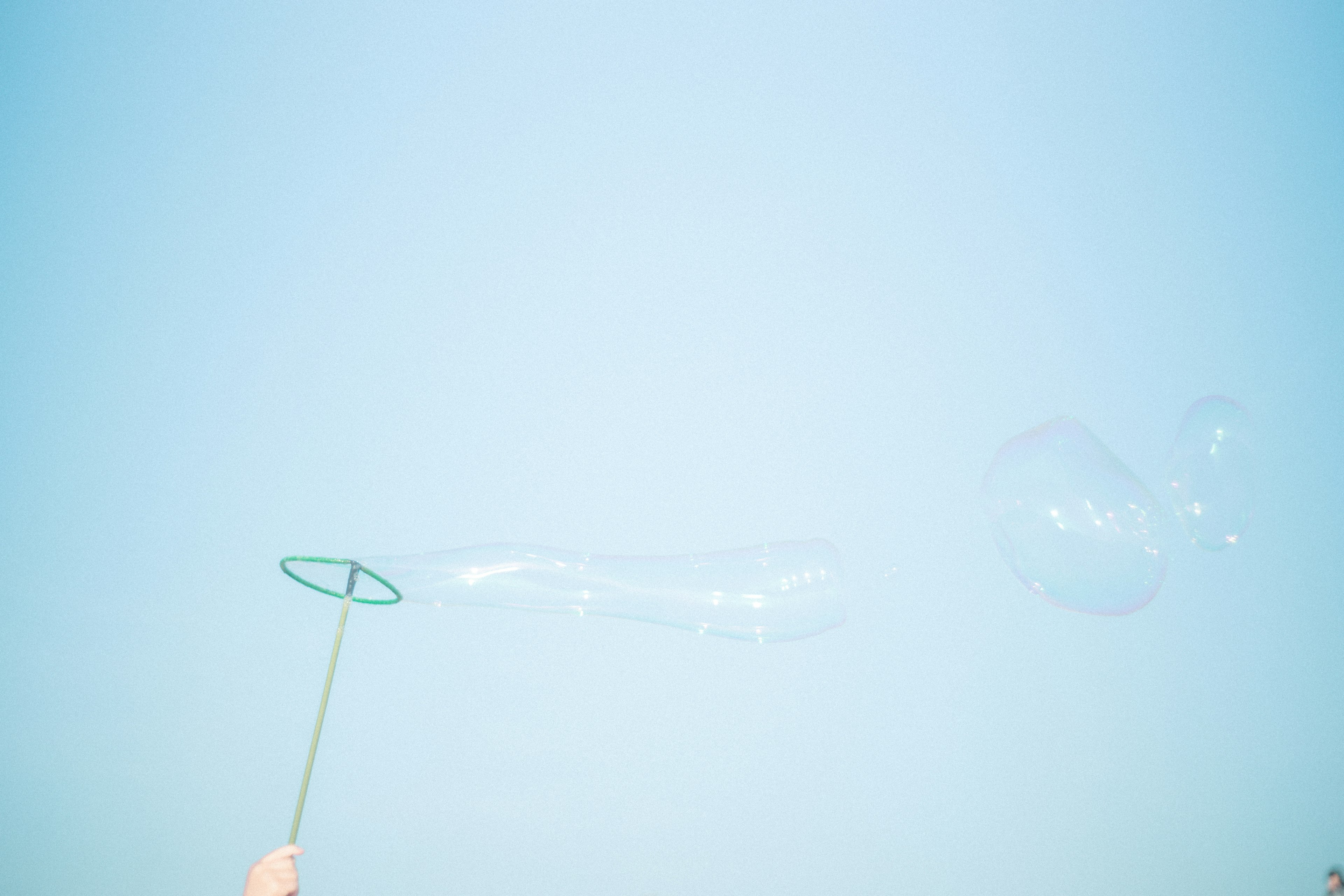 Hand creating a soap bubble against a clear blue sky