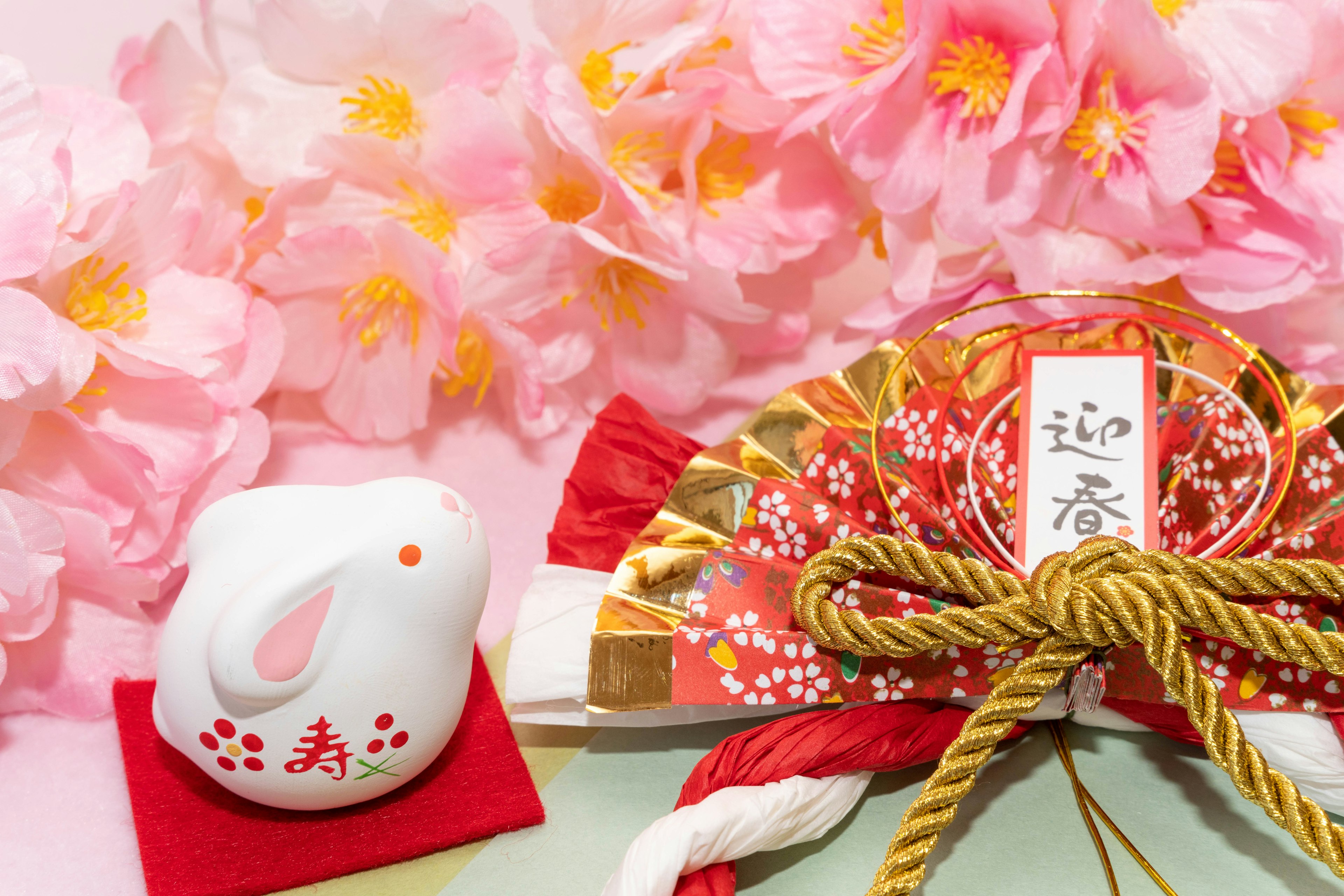 A white rabbit figurine beside a decorative fan with cherry blossoms in the background