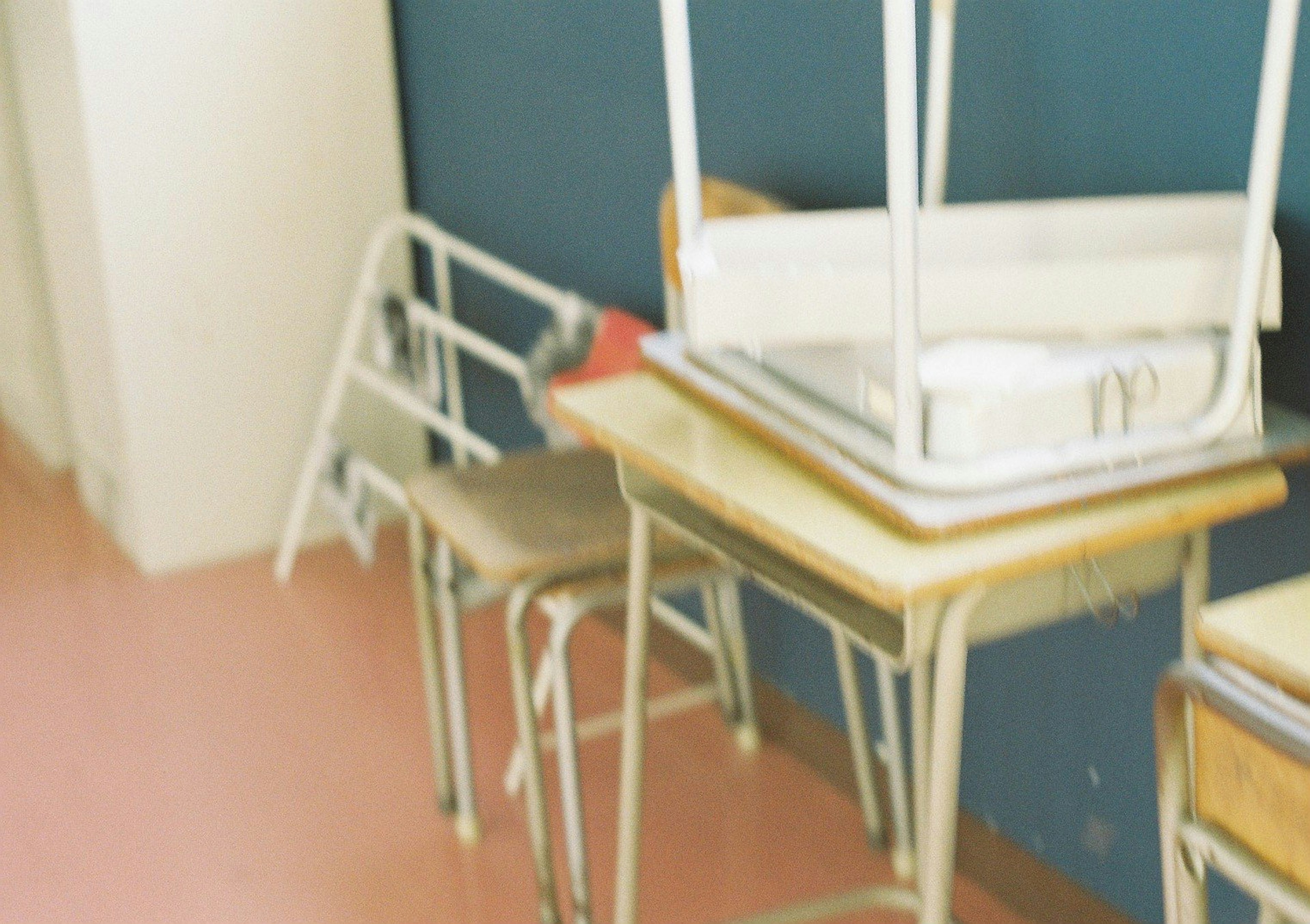 Escena de aula con sillas y escritorios apilados contra una pared azul y un suelo rosa