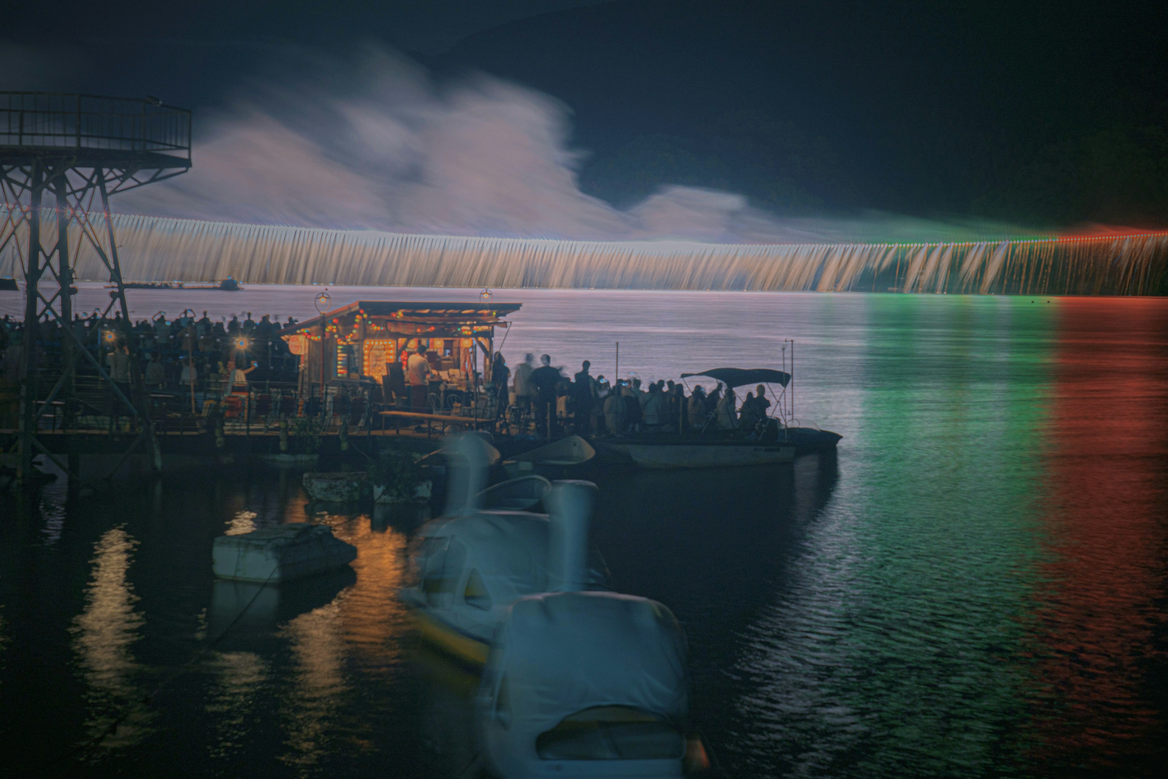 夜の水辺に集まる人々とカラフルなライトの滝