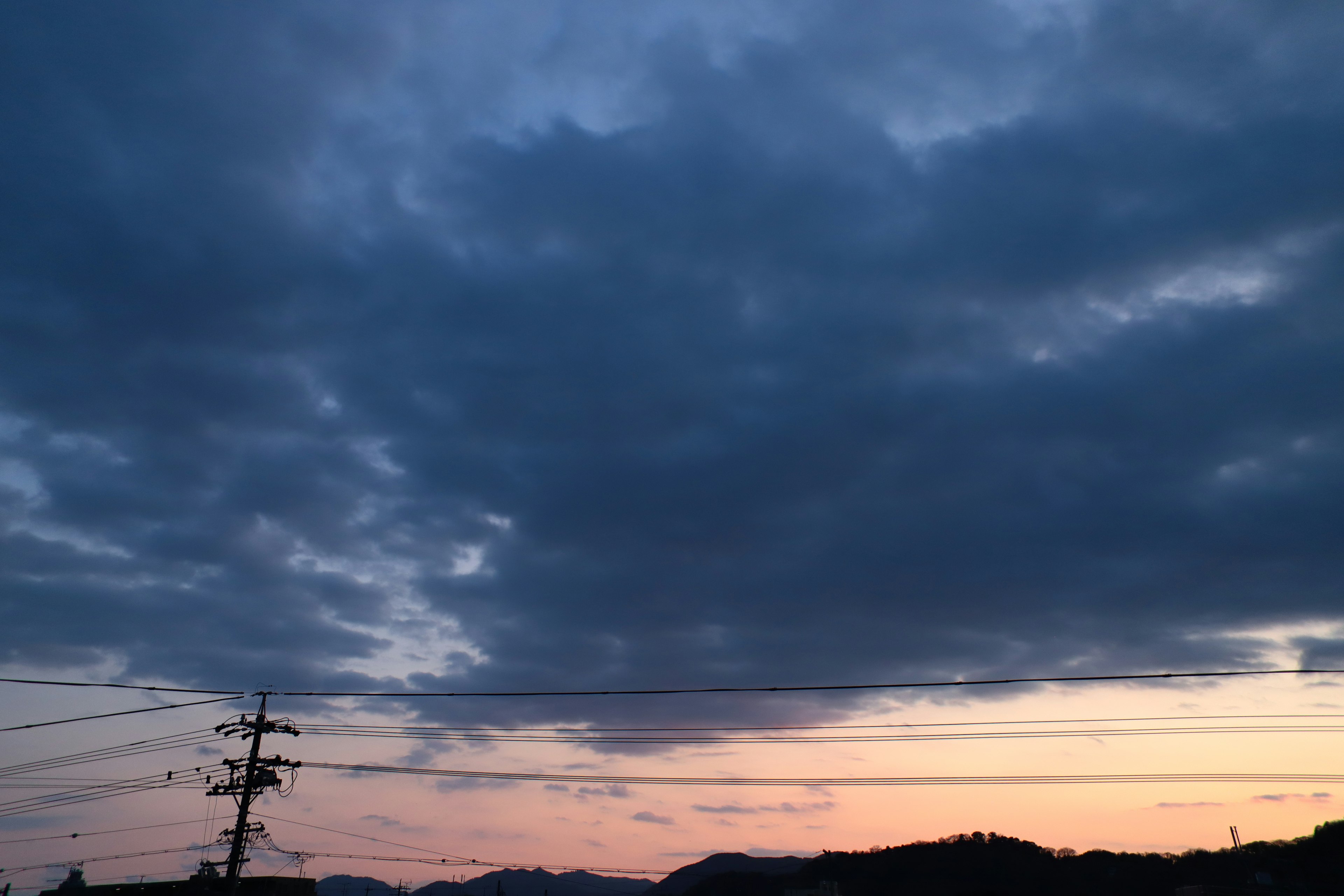 Dark clouds over a sunset sky with silhouettes of hills