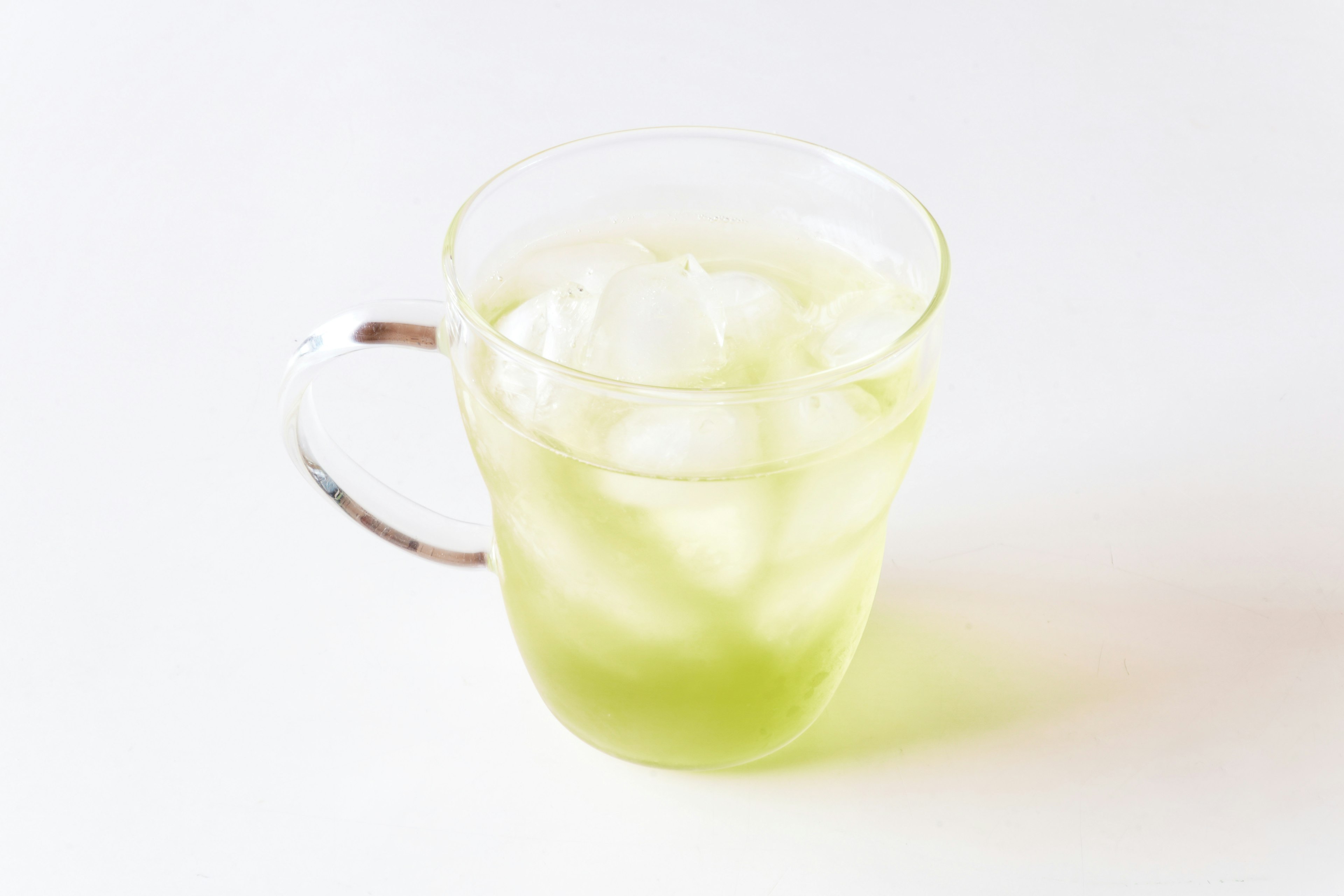 Transparent glass with a light green drink and ice cubes