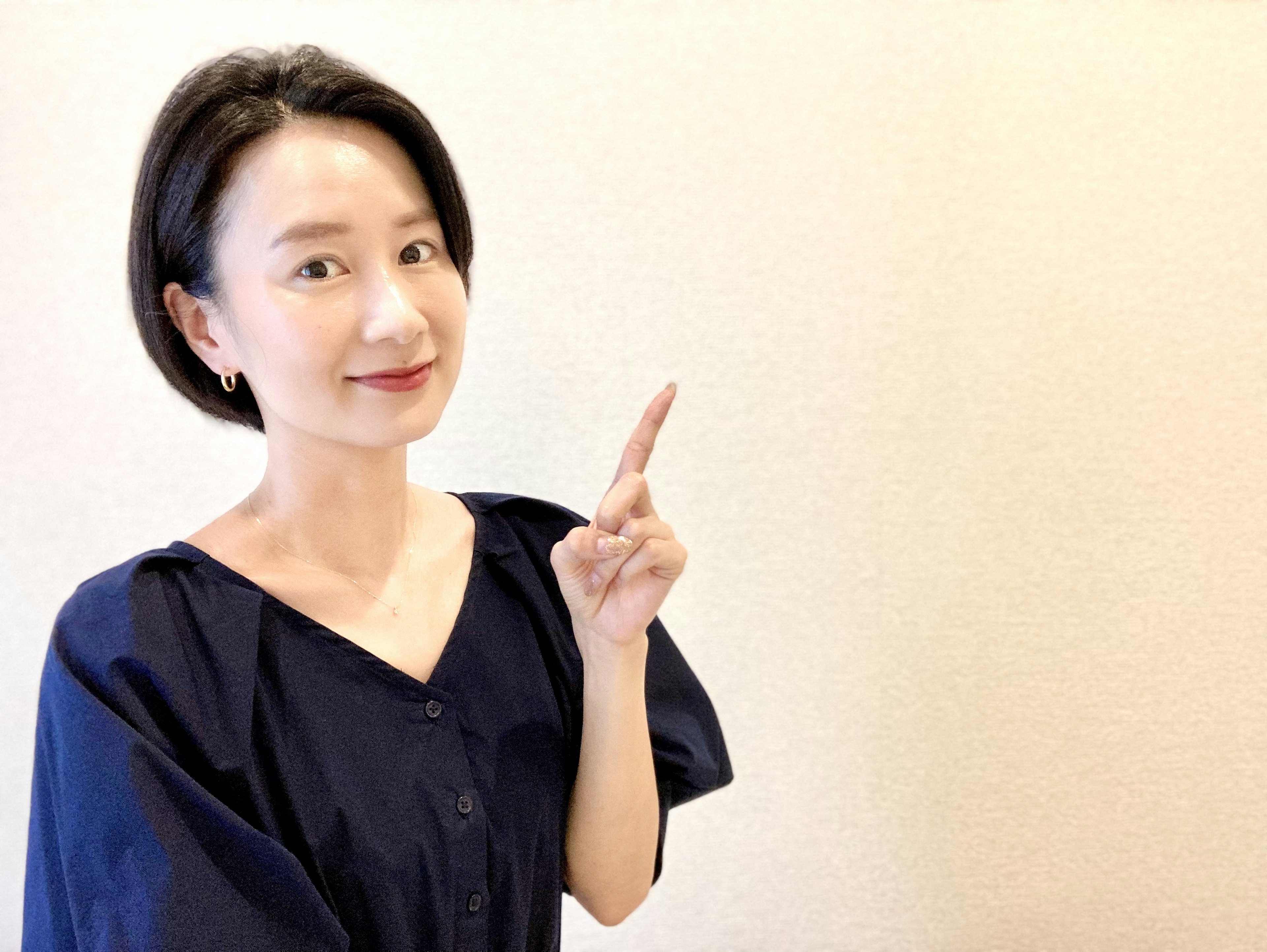 A woman smiling and pointing with one finger against a simple background