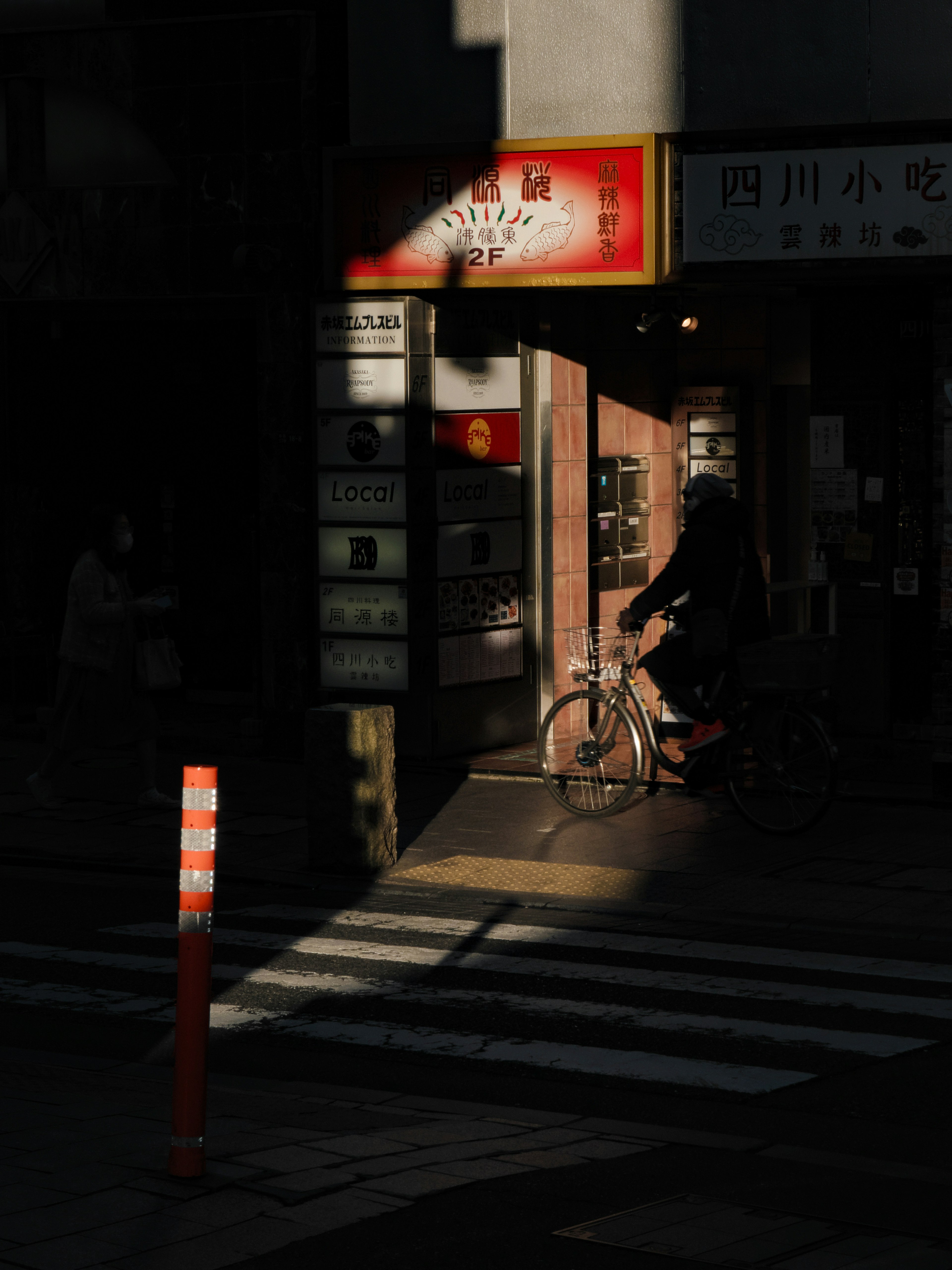 A scene of a person pushing a bicycle on a dark street with a prominent shop sign