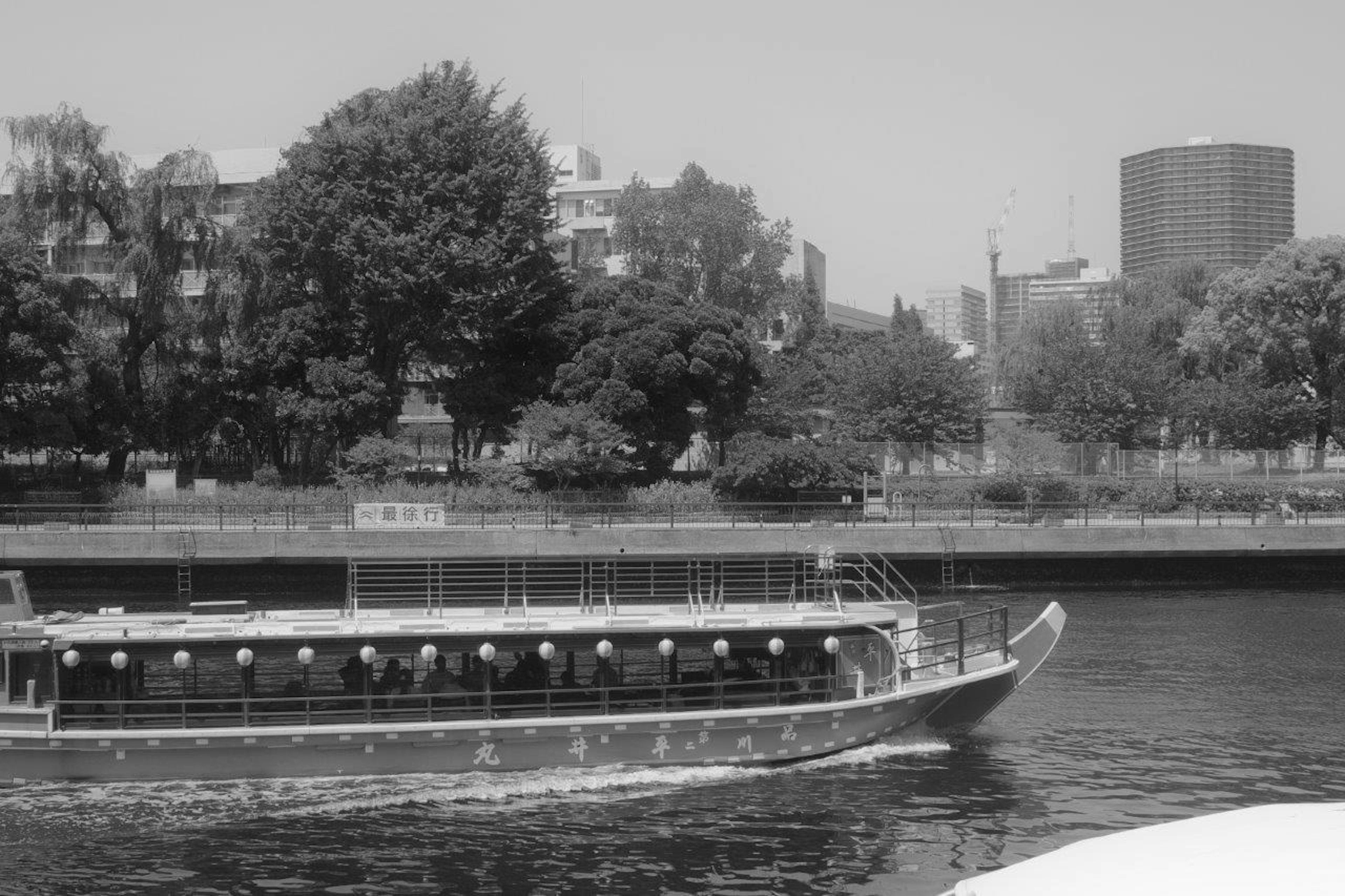 Black and white image of a boat navigating a river with lush greenery