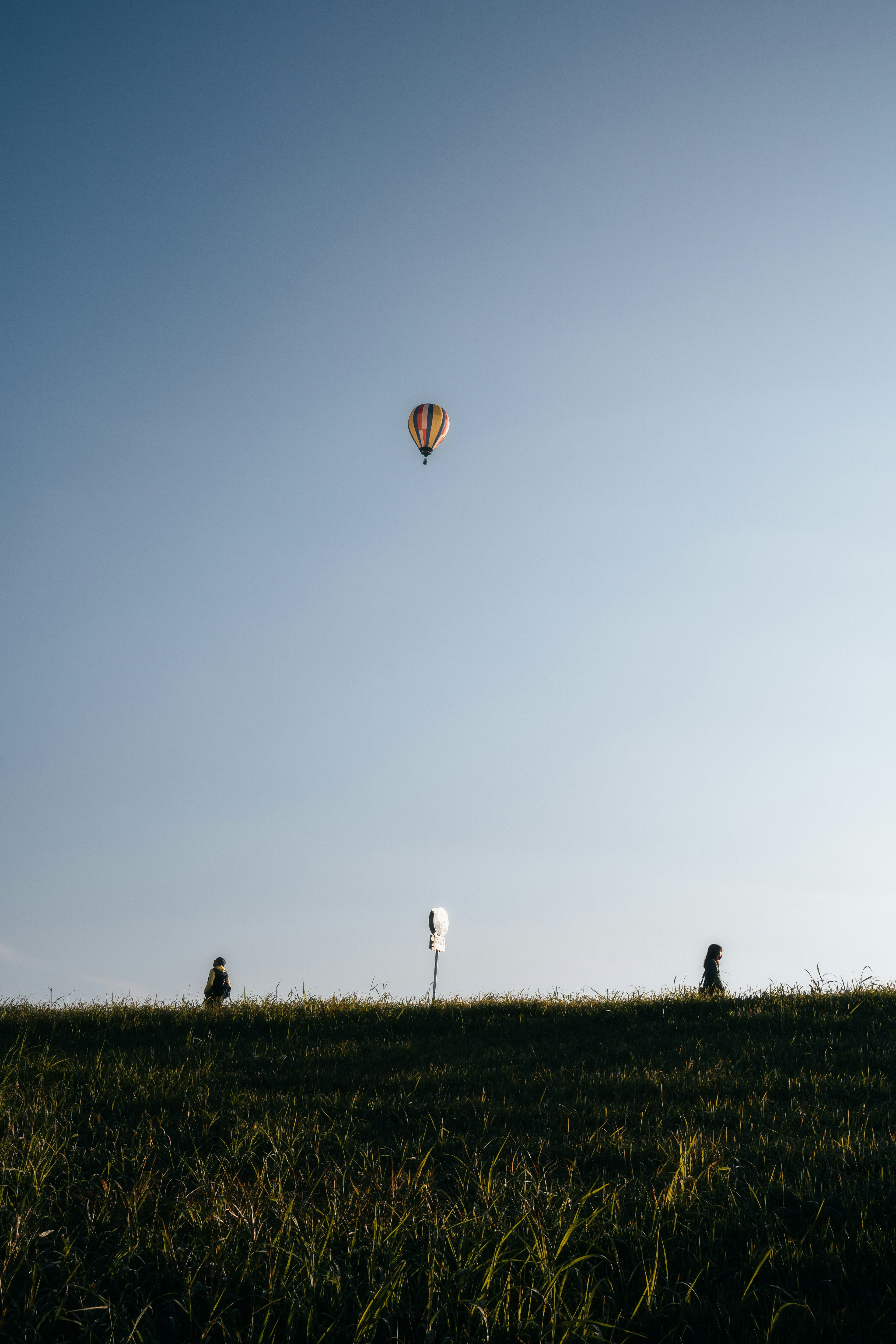 Sebuah balon udara panas mengapung di langit dengan orang-orang berdiri di atas rumput