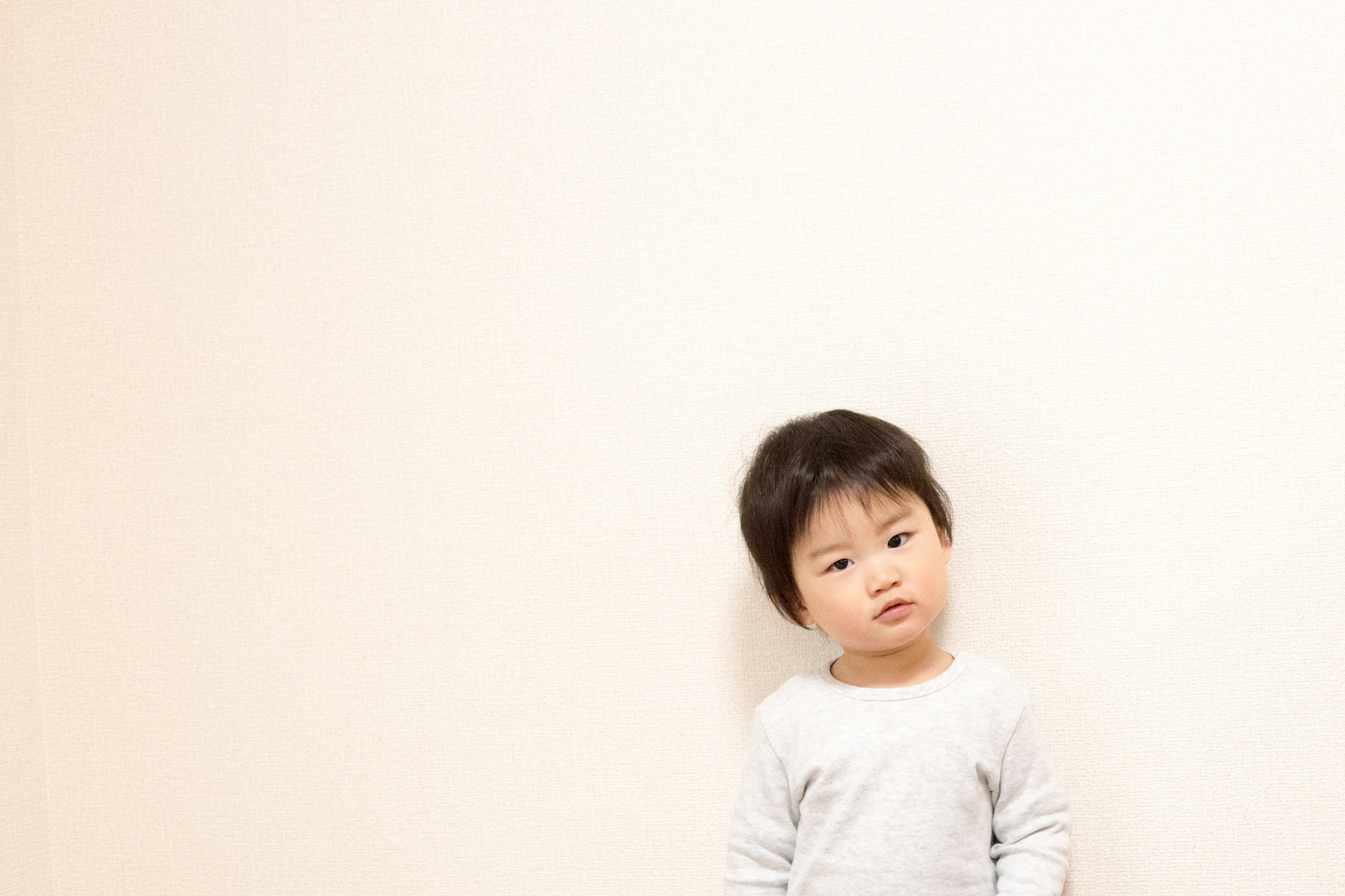 A small boy standing against a light-colored wall