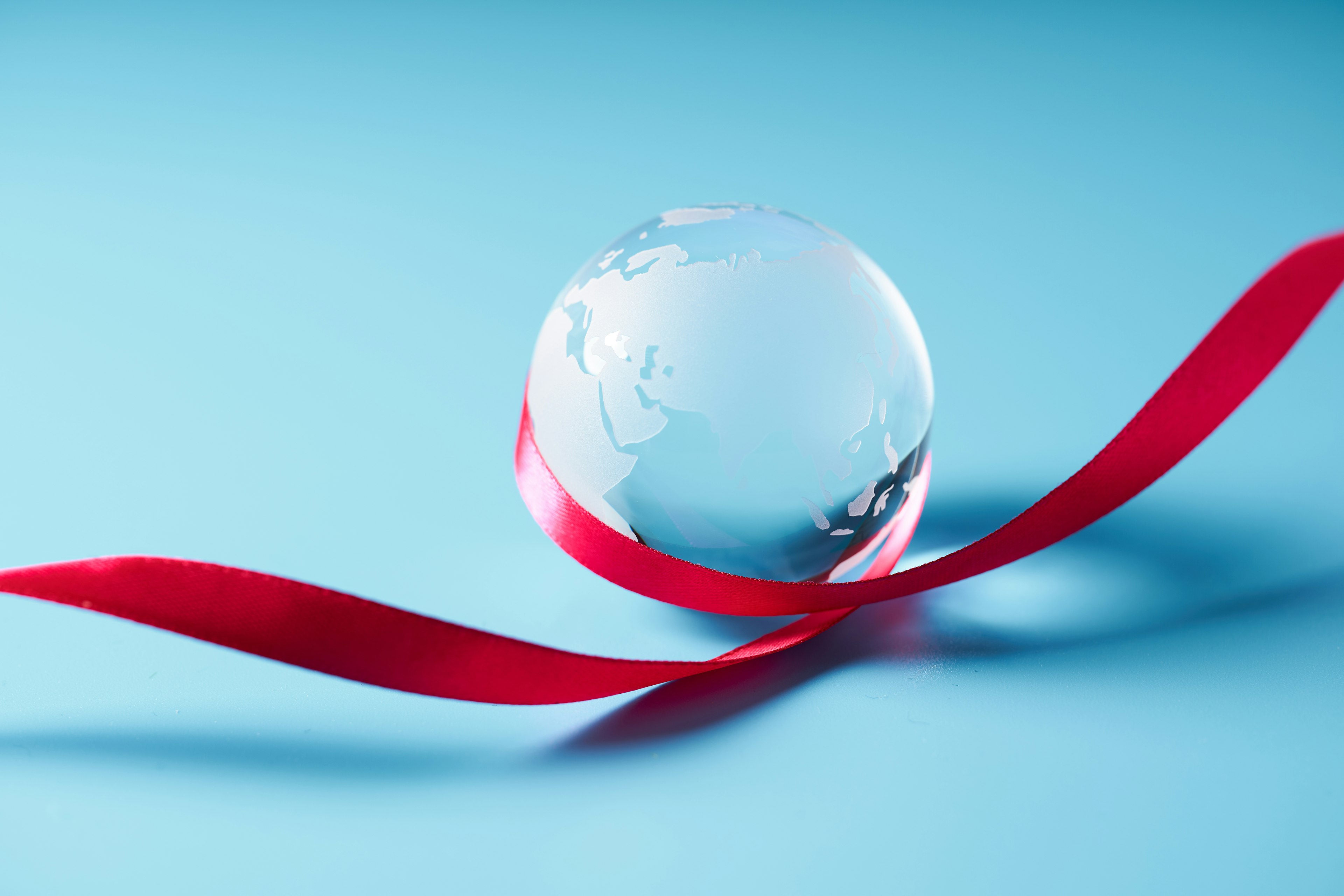 A transparent globe wrapped in a red ribbon on a blue background