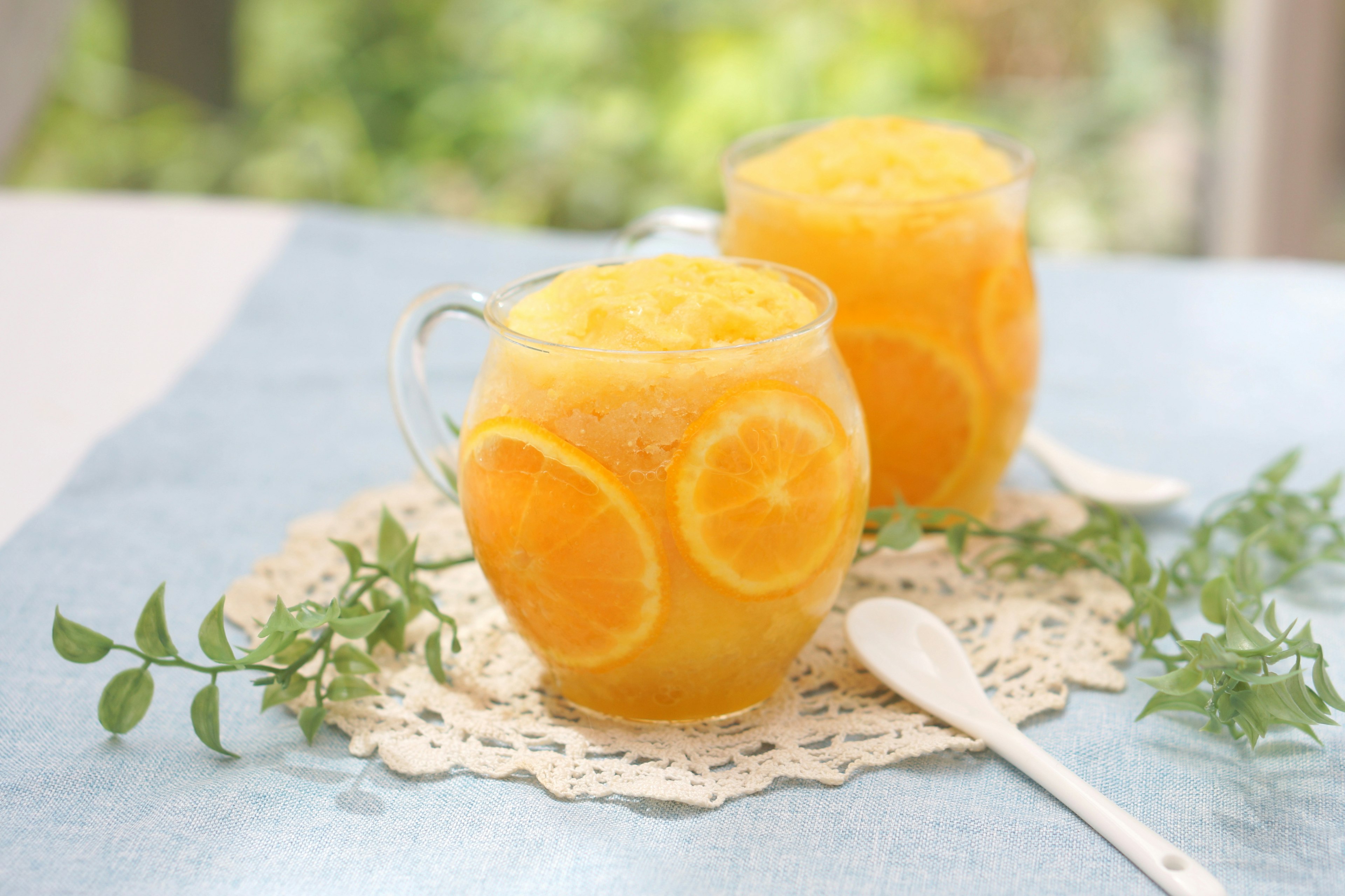 Zwei Gläser mit Orangensmoothie und Orangenscheiben auf einem Spitzen-Tischdecken