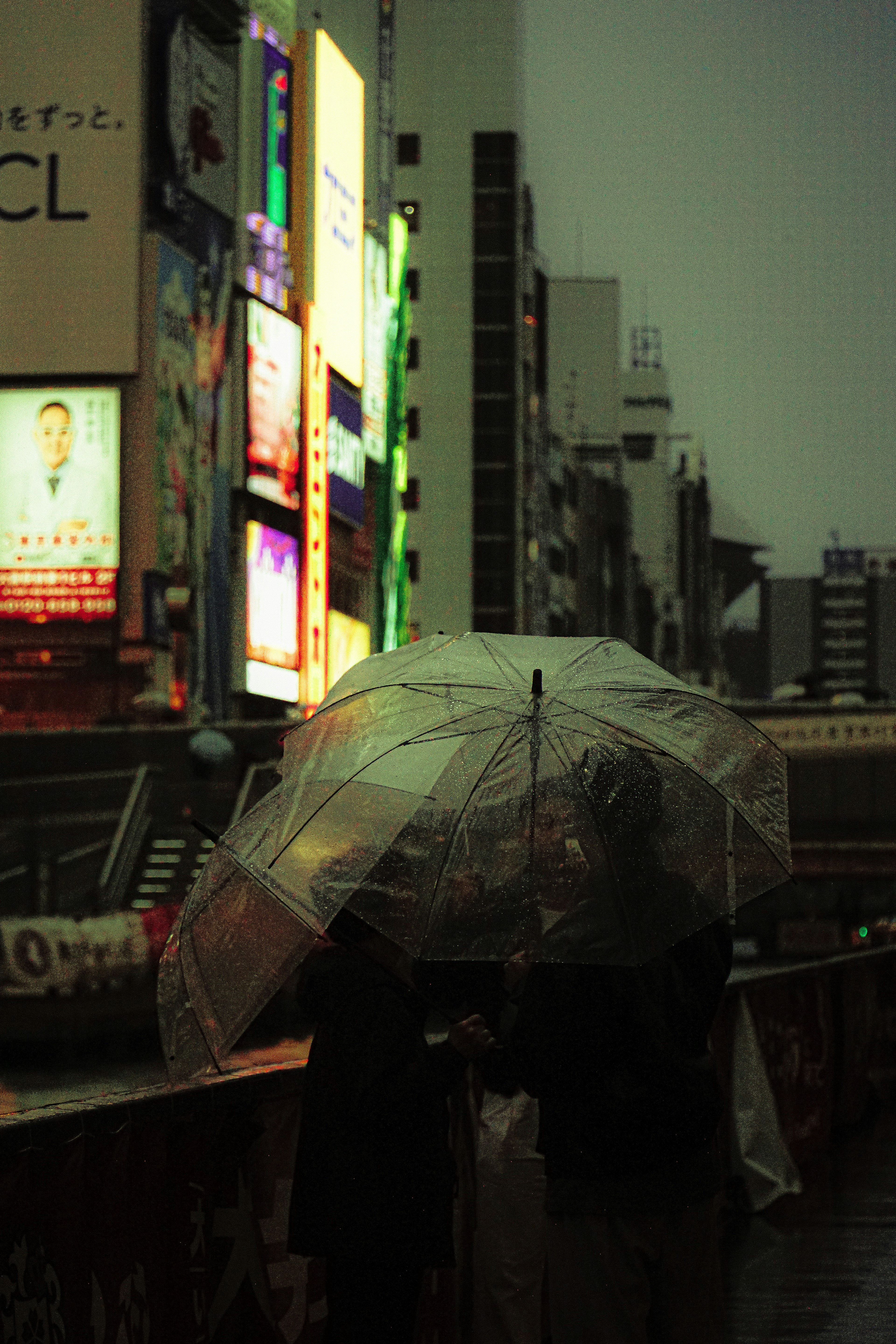 在雨中，拿著透明雨傘的人們站在明亮的城市廣告牌前