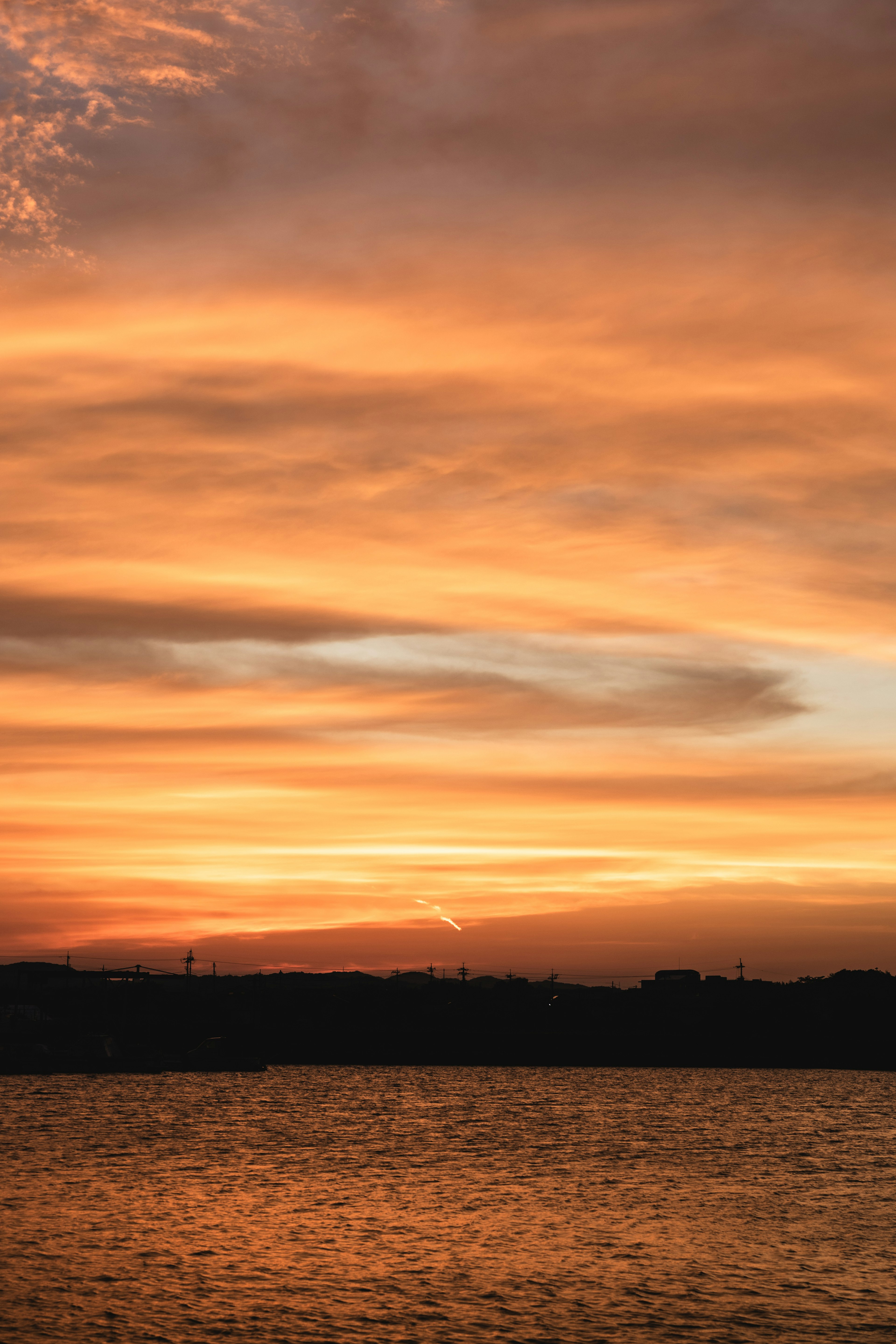 Tramonto vibrante con nuvole arancioni e rosa sopra una superficie d'acqua calma