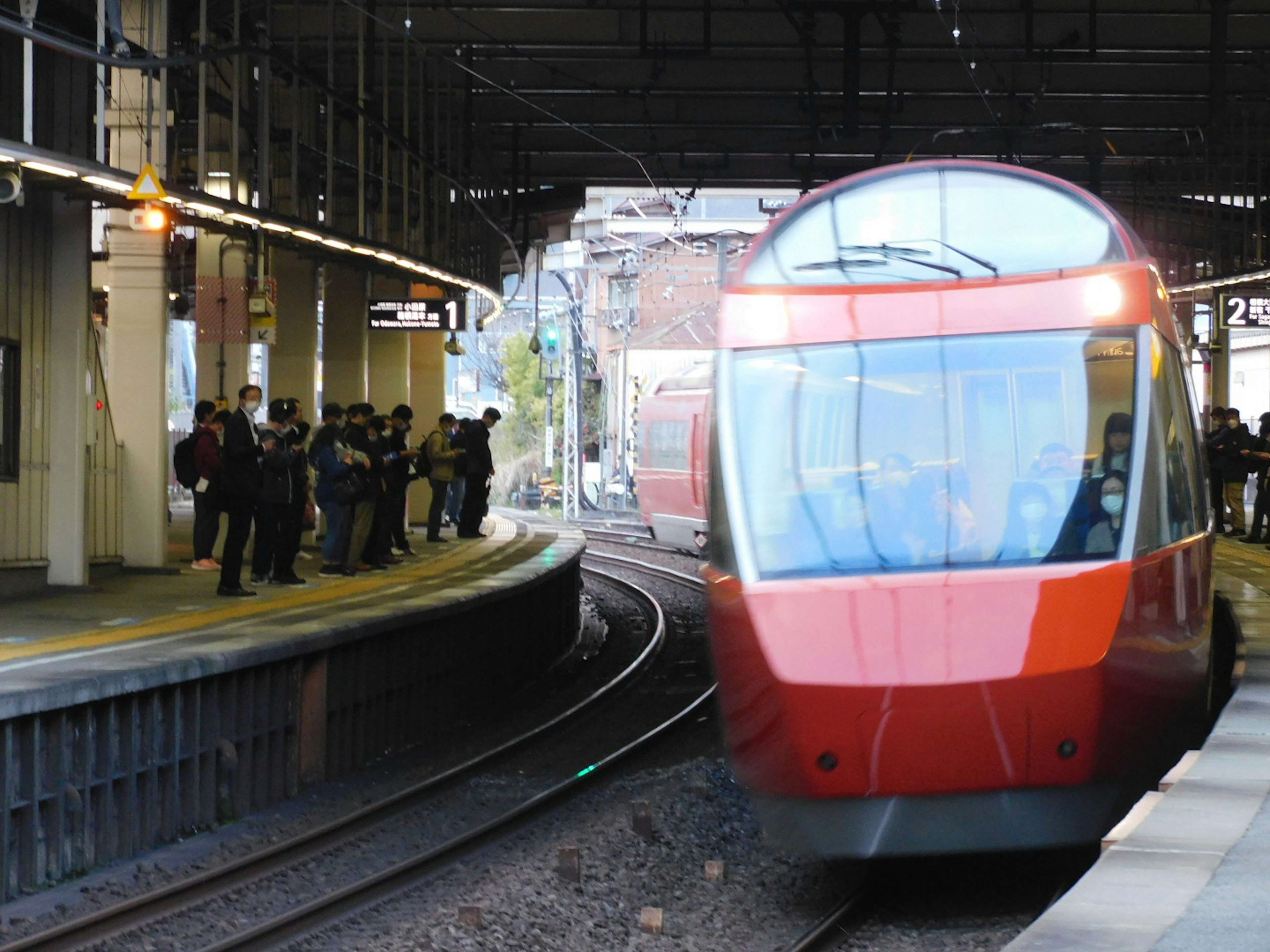 Red train approaching the station with waiting passengers