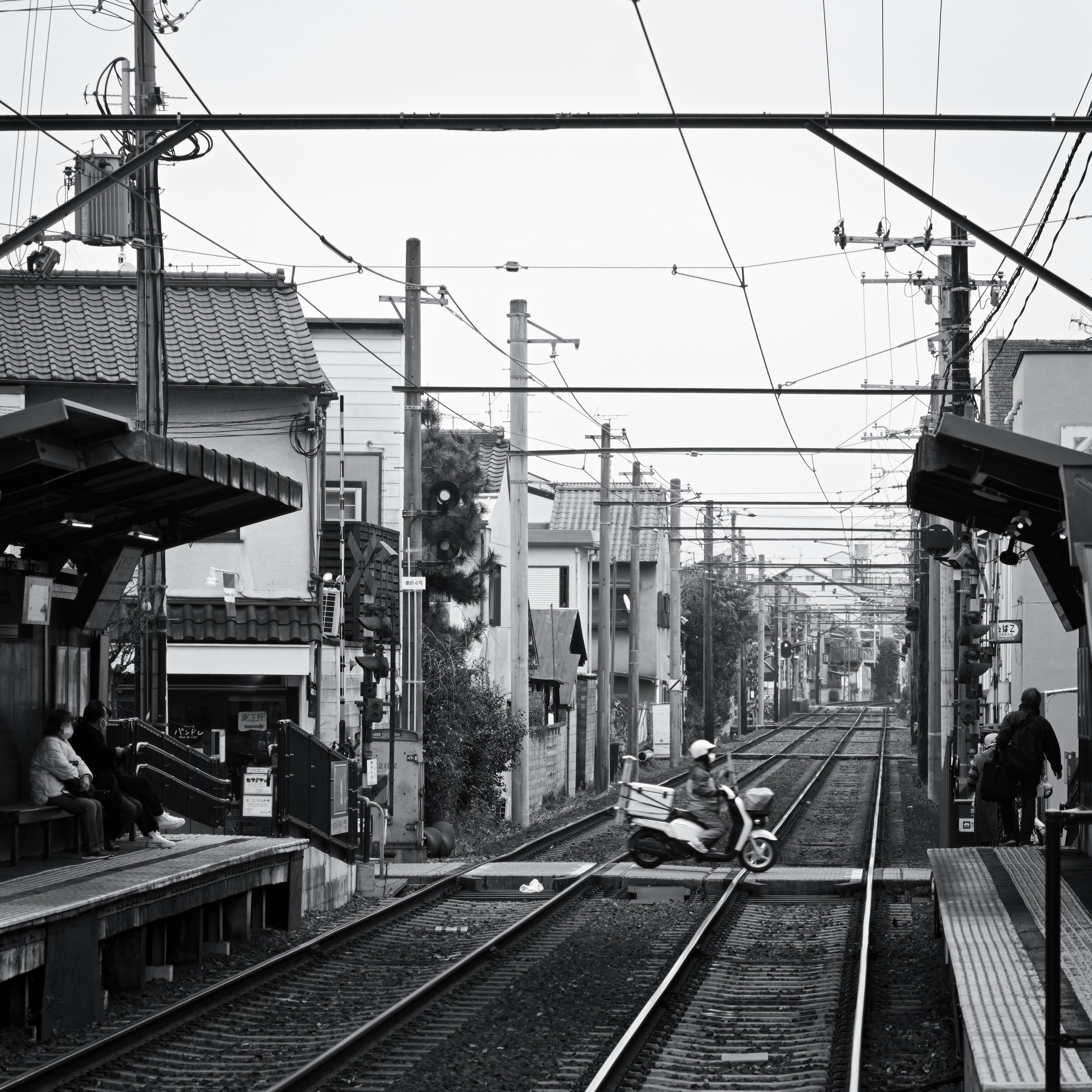 Image en noir et blanc d'une gare de ville avec un scooter traversant la voie ferrée