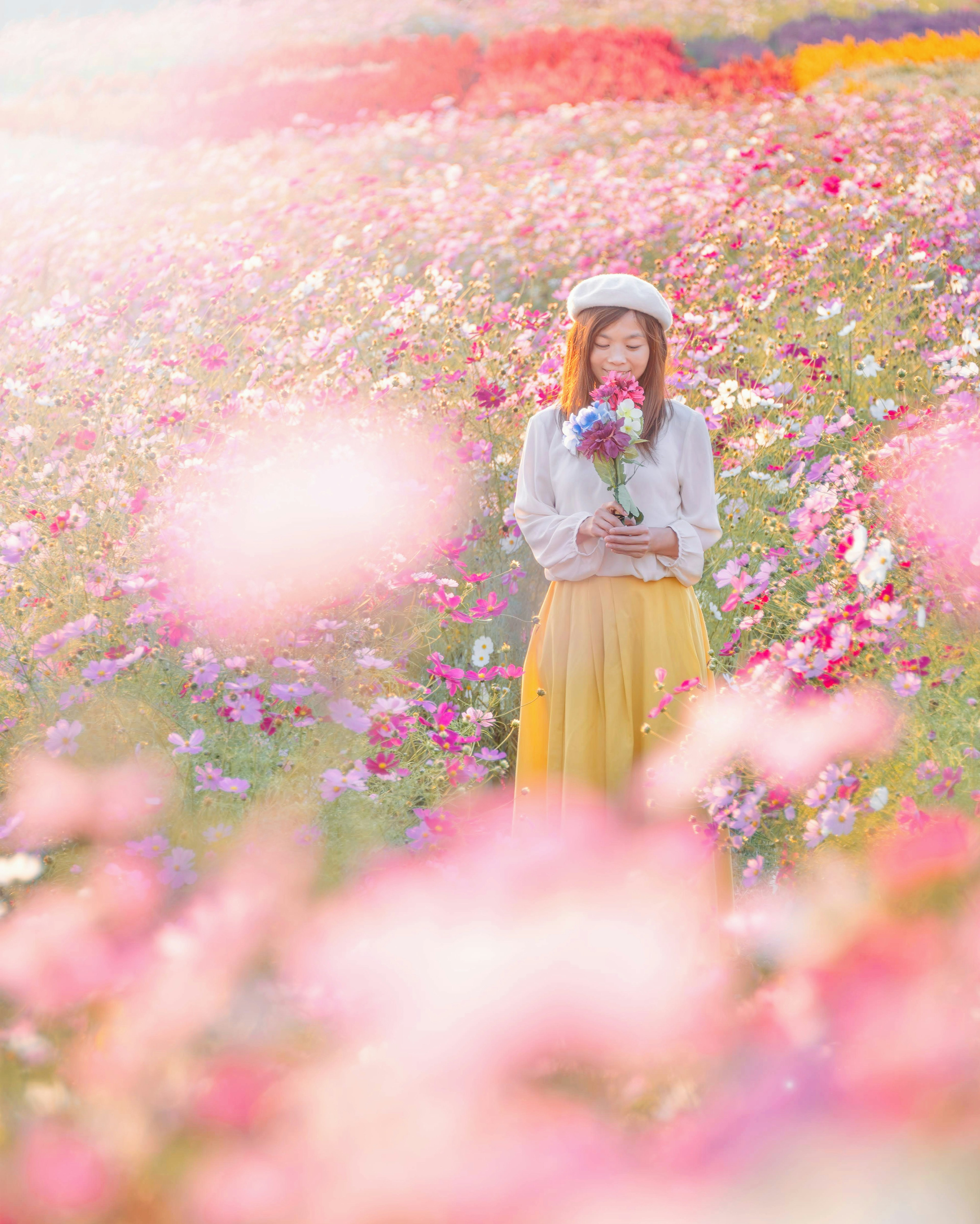 꽃밭에 서 있는 여성 꽃다발을 들고 노란 치마와 흰색 상의를 입고 있음