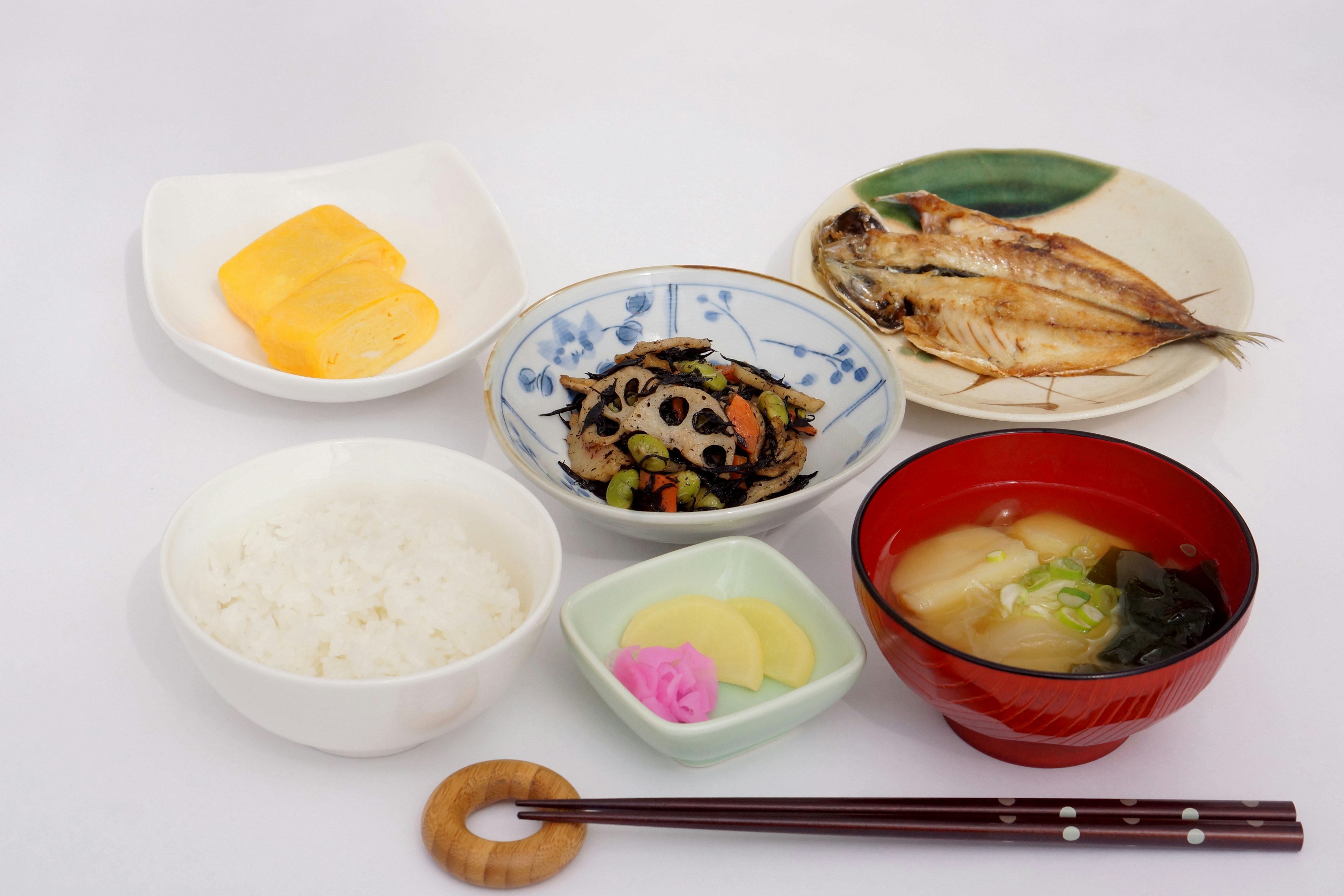 Traditional Japanese breakfast arrangement with white rice, miso soup, grilled fish, simmered vegetables, pickles, and tamagoyaki