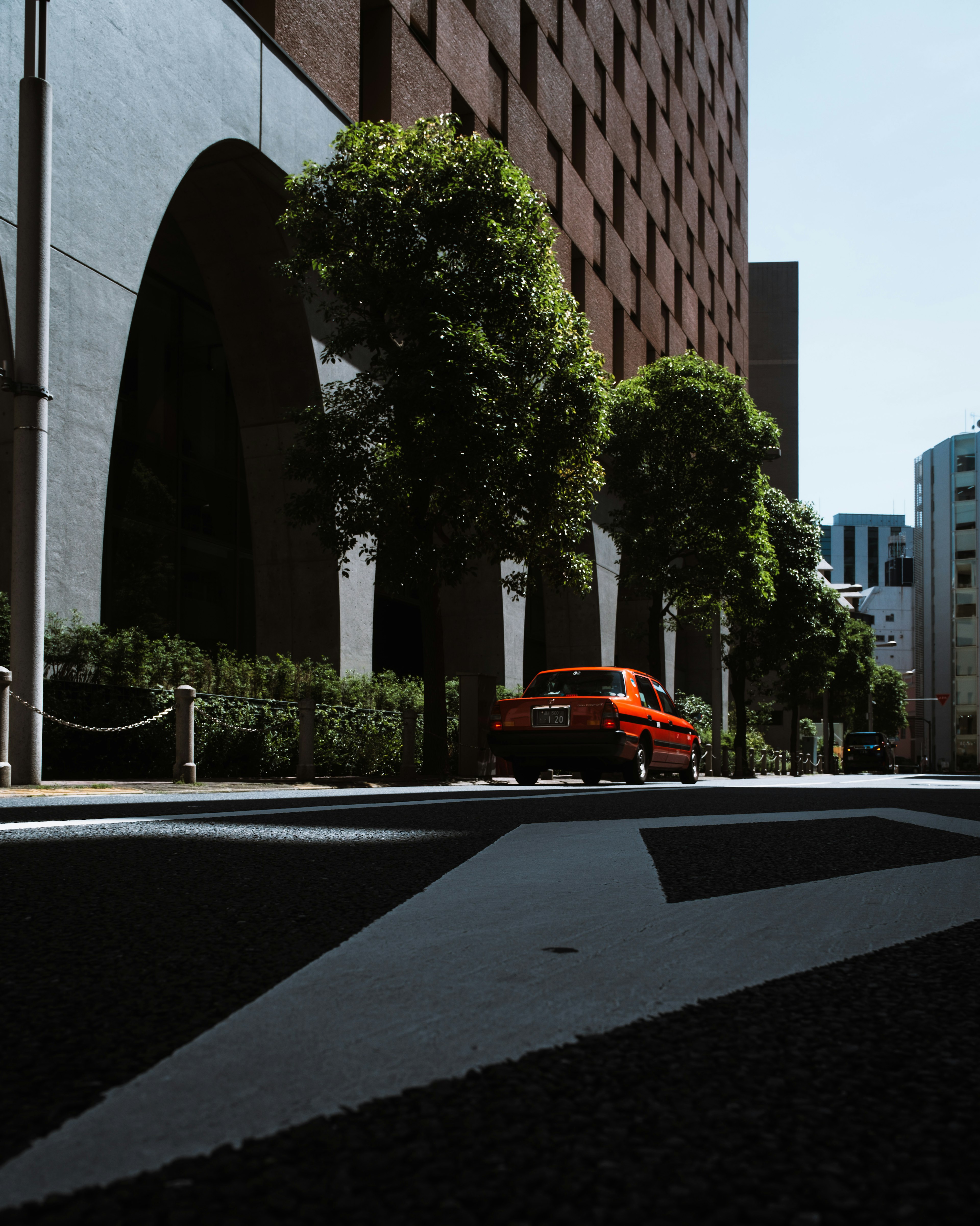 Un'auto rossa parcheggiata sulla strada con edifici ad arco e alberi verdi in vista