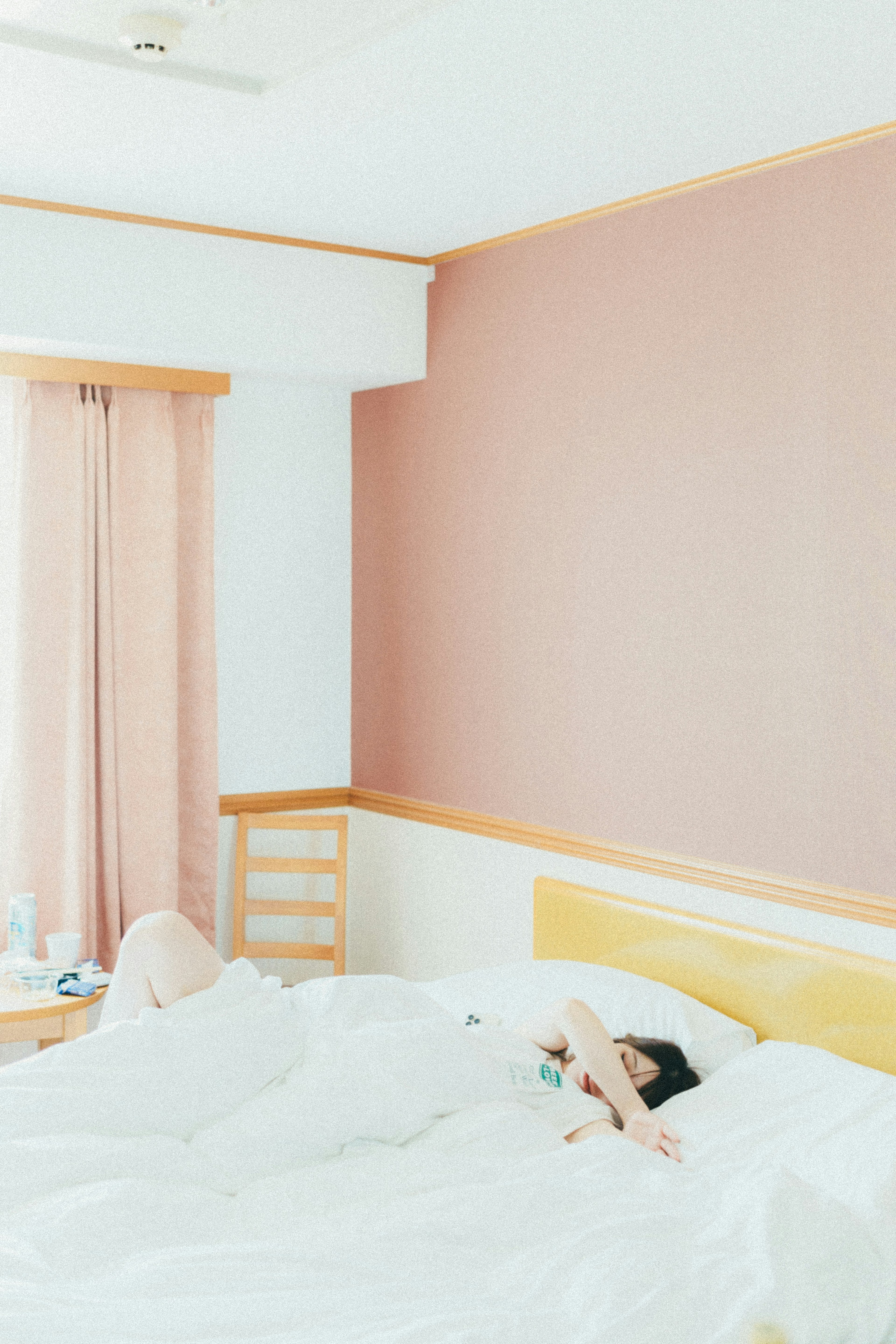 A tranquil bedroom featuring a person sleeping and a soft pink wall