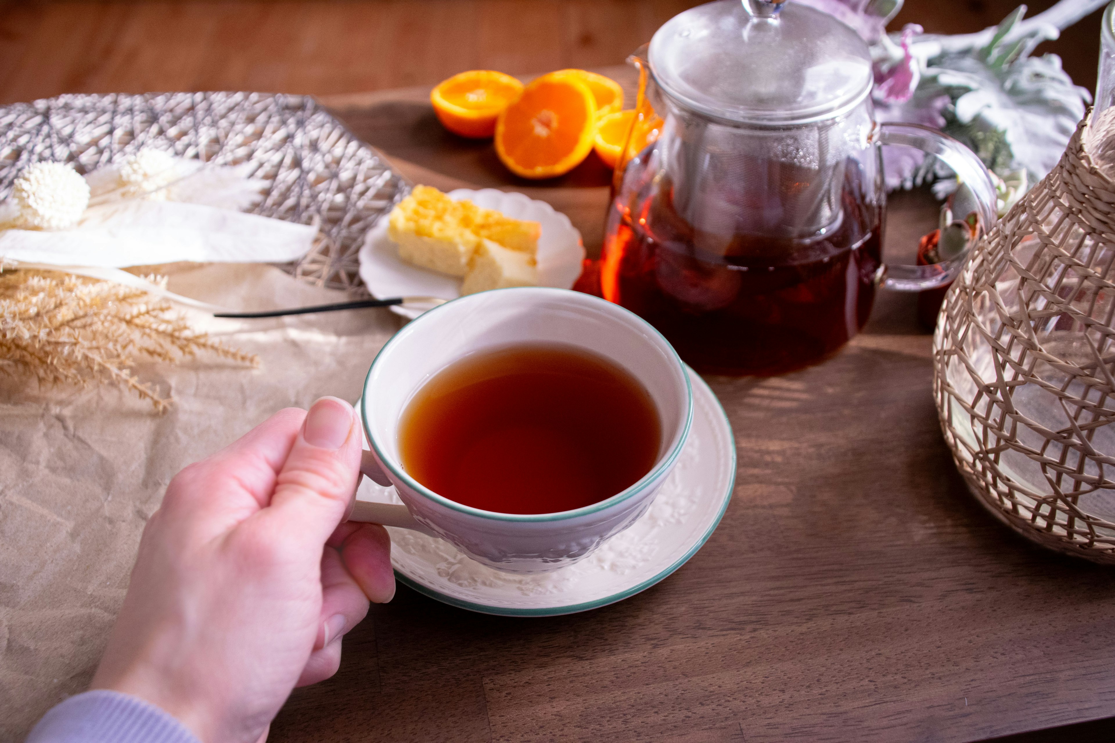 Main tenant une tasse de thé noir avec une théière à proximité contenant des oranges et du beurre