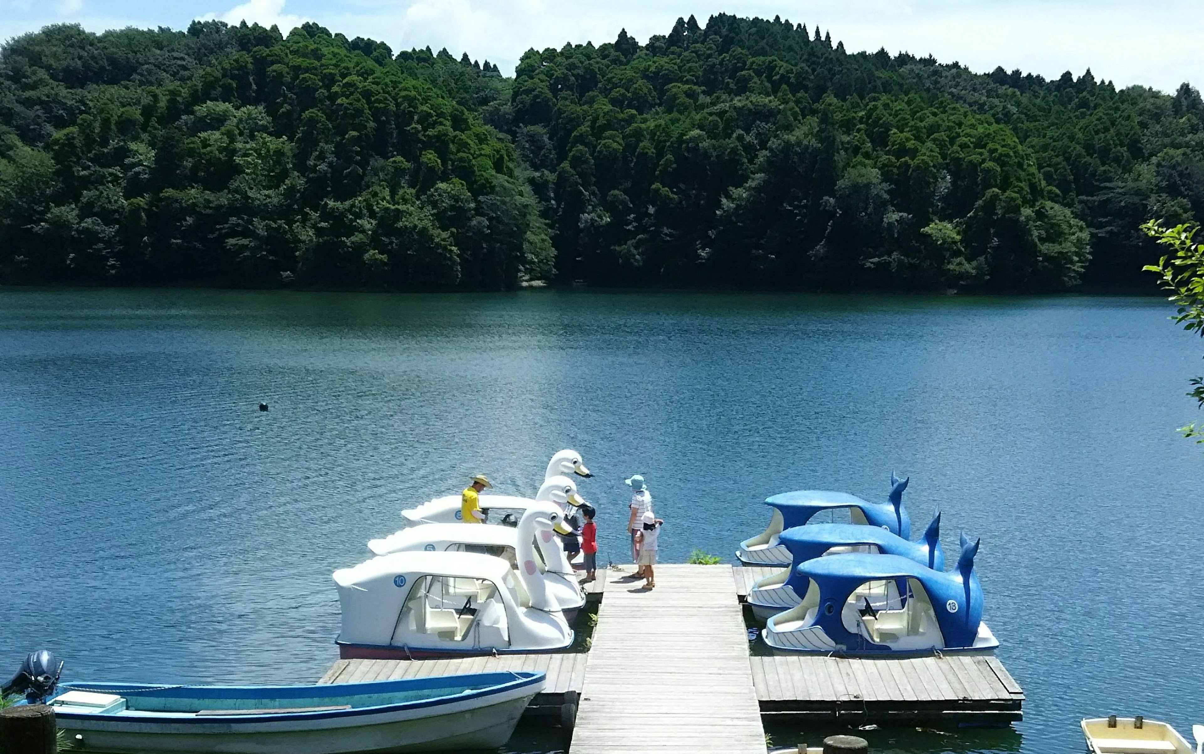 Menschen genießen einen sonnigen Tag an einem Dock mit blauen Booten an einem See