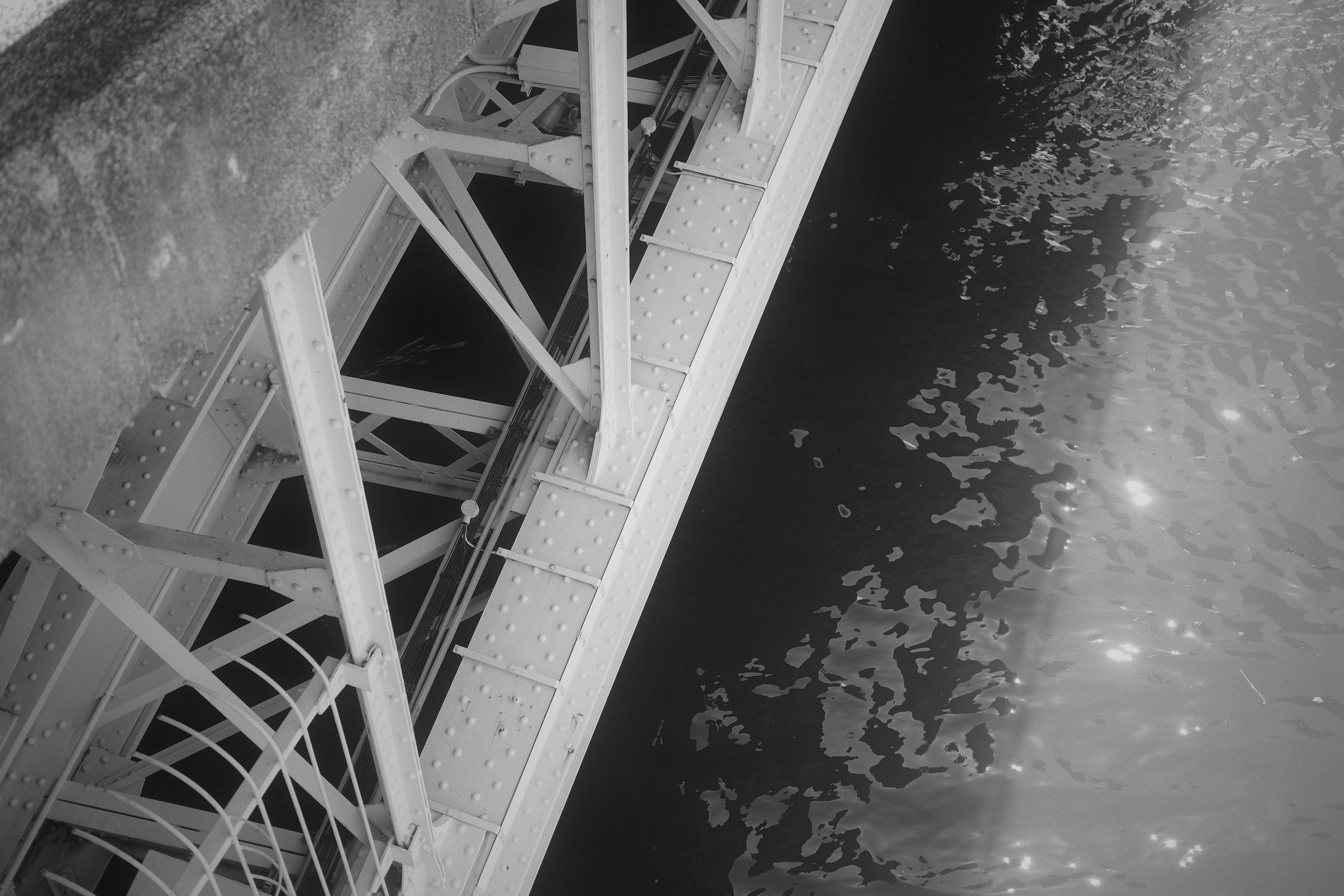 Image en noir et blanc montrant la structure d'un pont au-dessus de la surface de l'eau