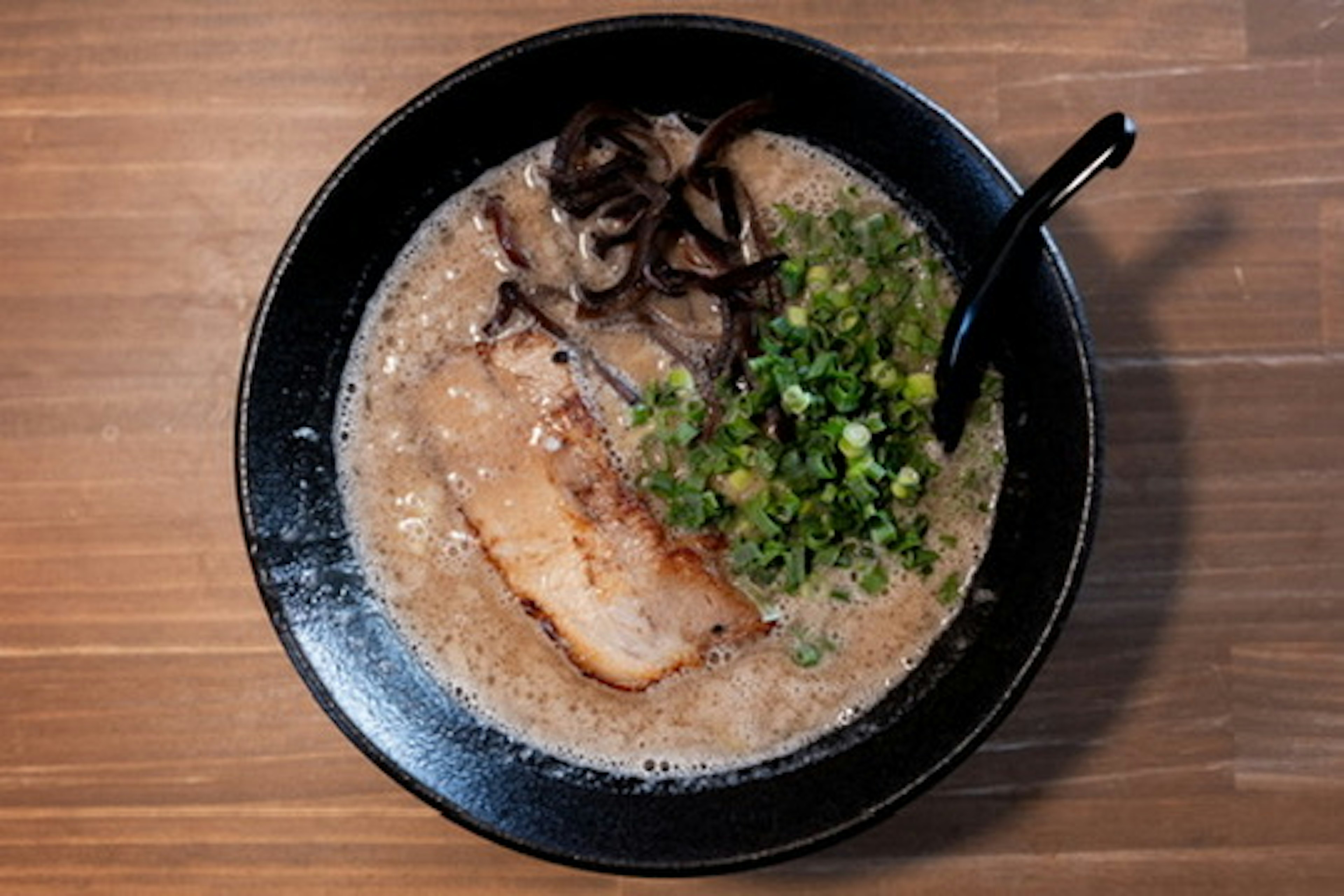 Soupe de ramen dans un bol noir garnie de porc tranché et d'oignons verts