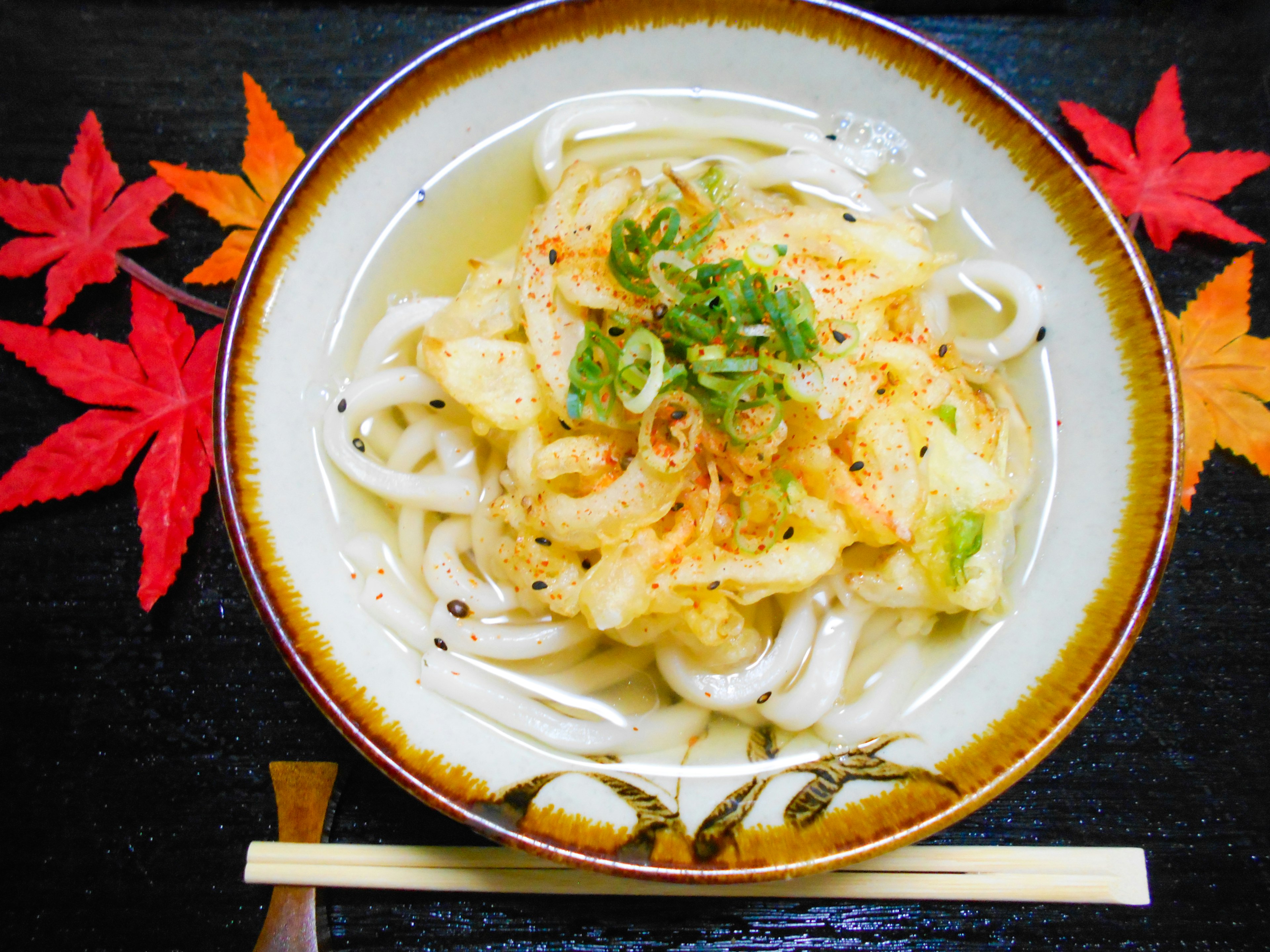 Ciotola di udon caldo con cipolle verdi e cavolo circondata da foglie d'autunno