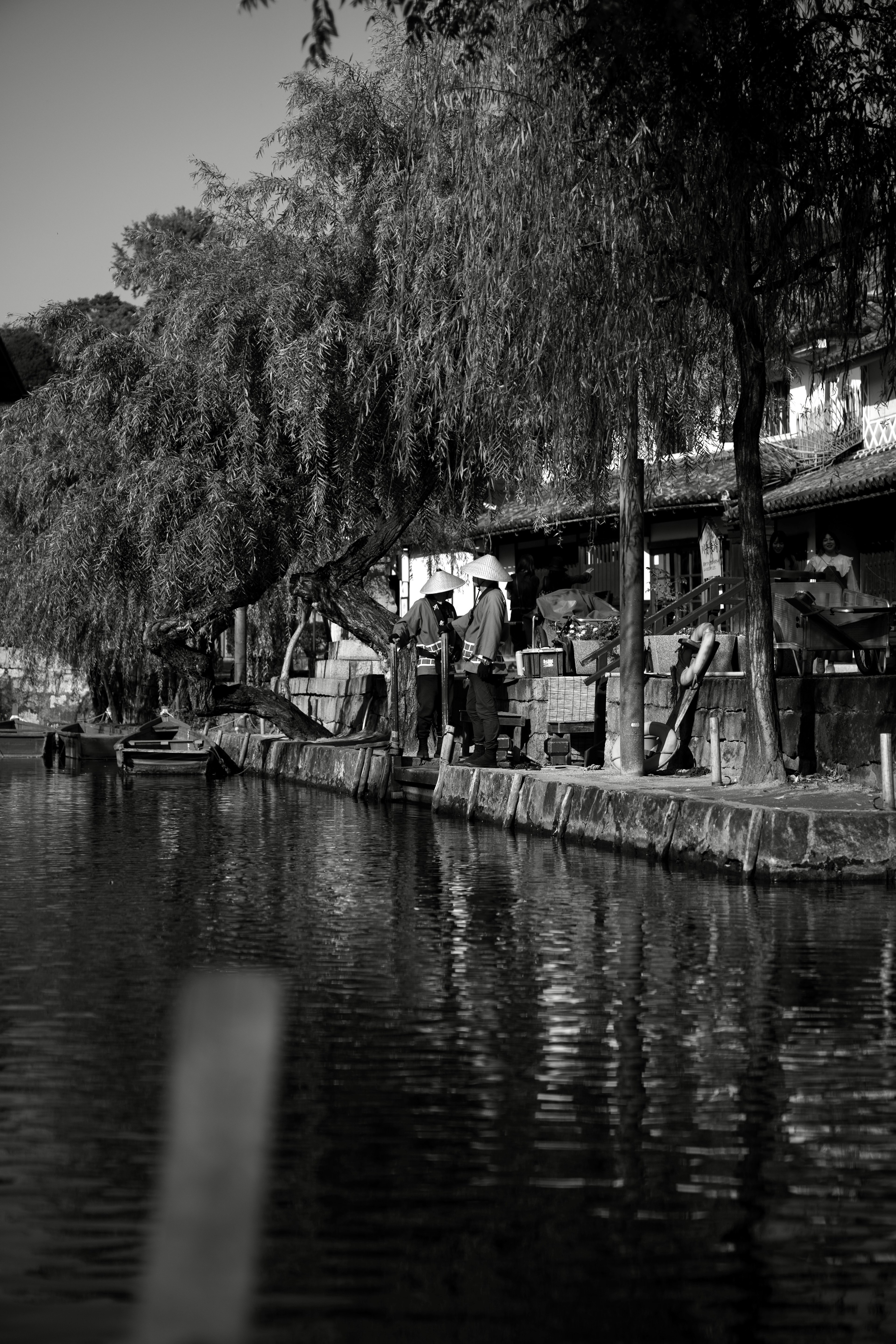 Escena en blanco y negro junto al río con árboles y un cobertizo