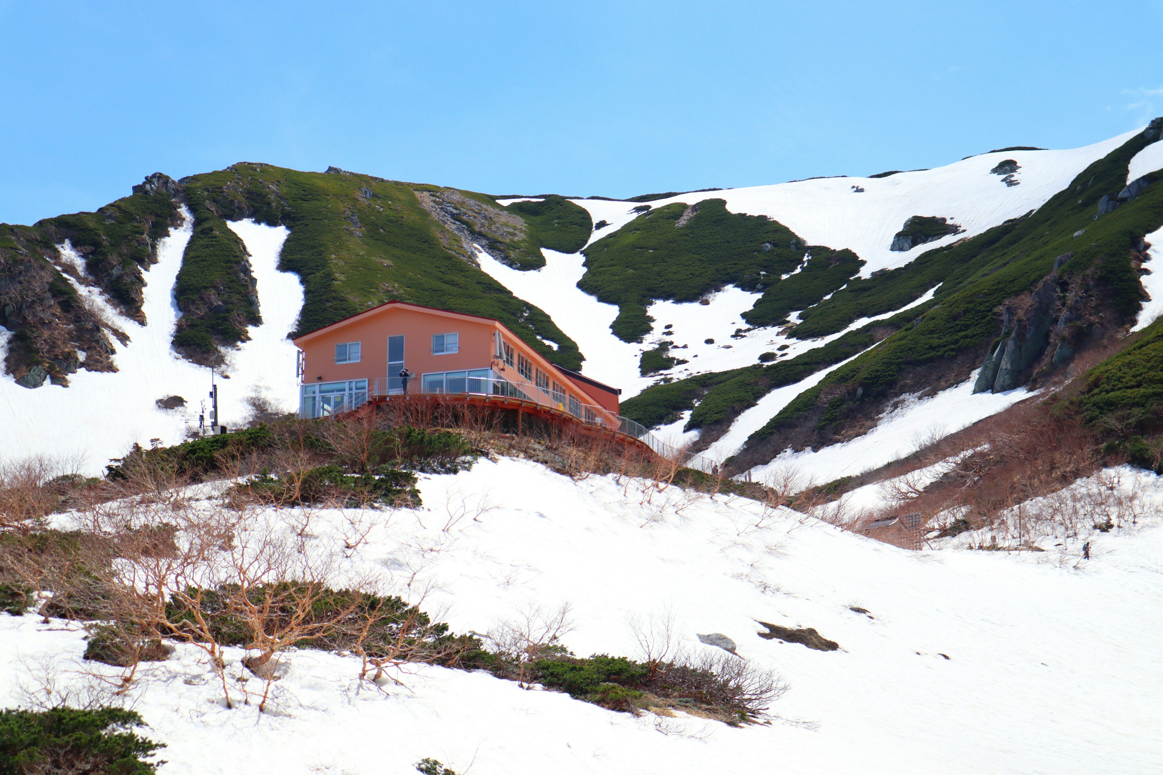 Una casa roja en una pendiente montañosa nevada con hierba verde