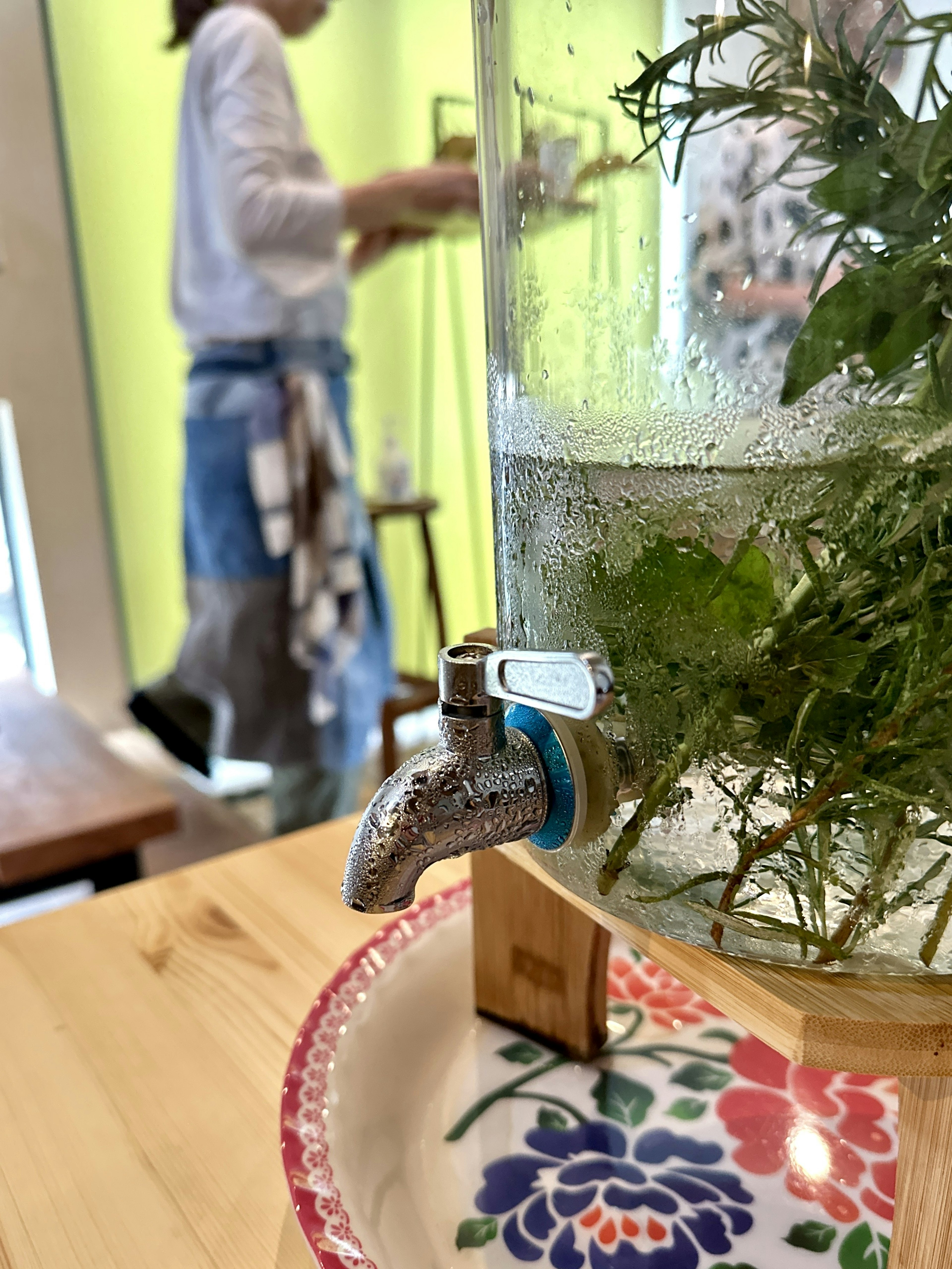 Glass container with water and floating herbs next to a faucet