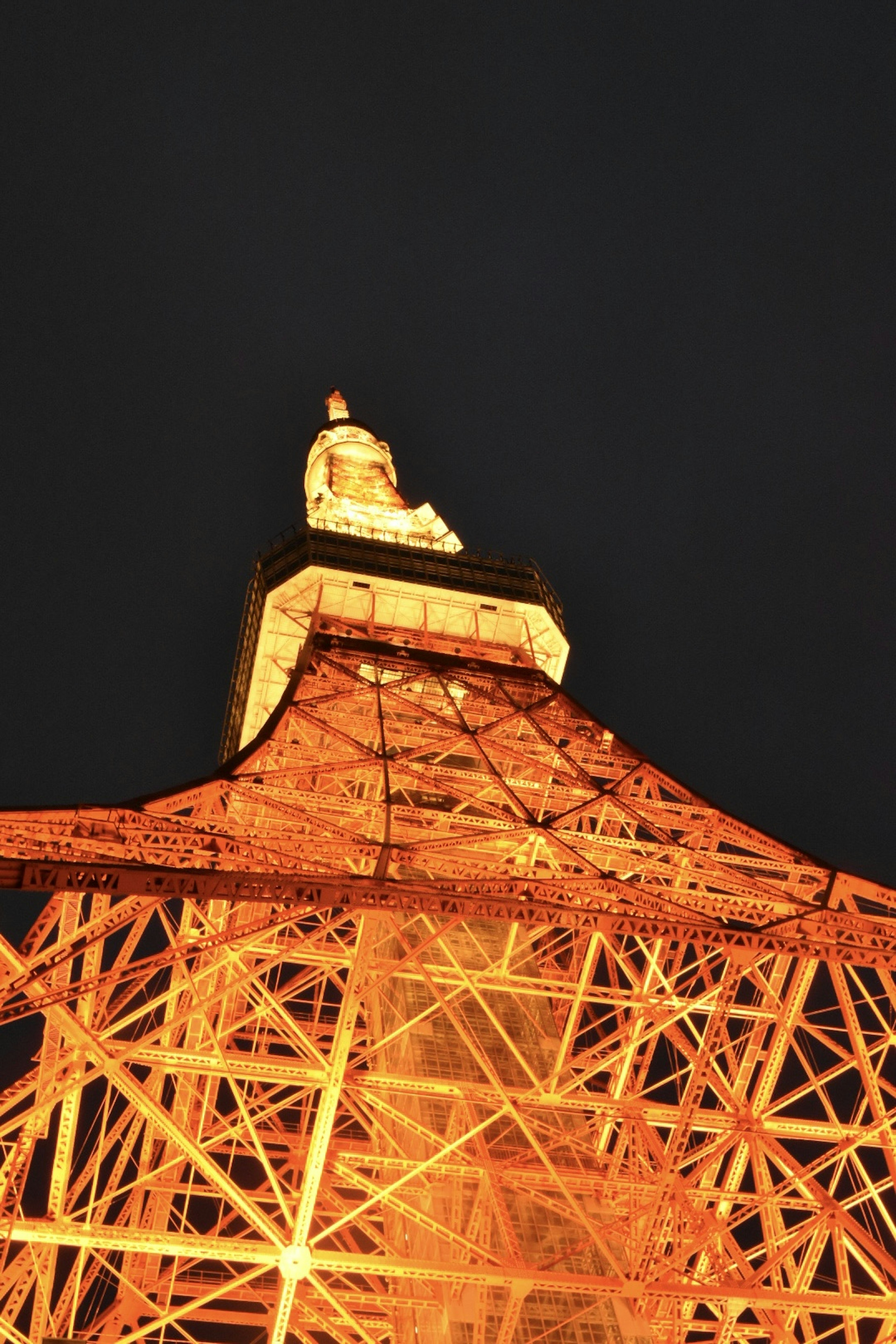 Photo of Tokyo Tower viewed from below at night showcasing its glowing orange structure