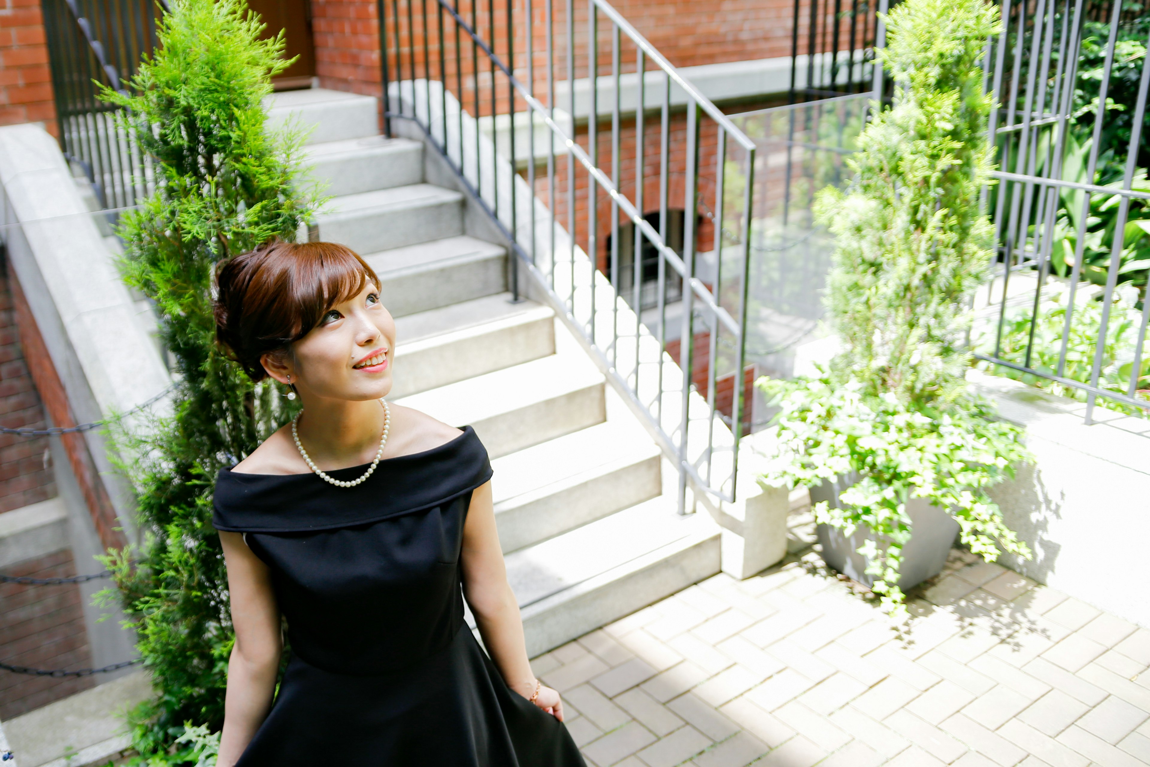 Woman in a black dress standing by stairs smiling surrounded by green plants