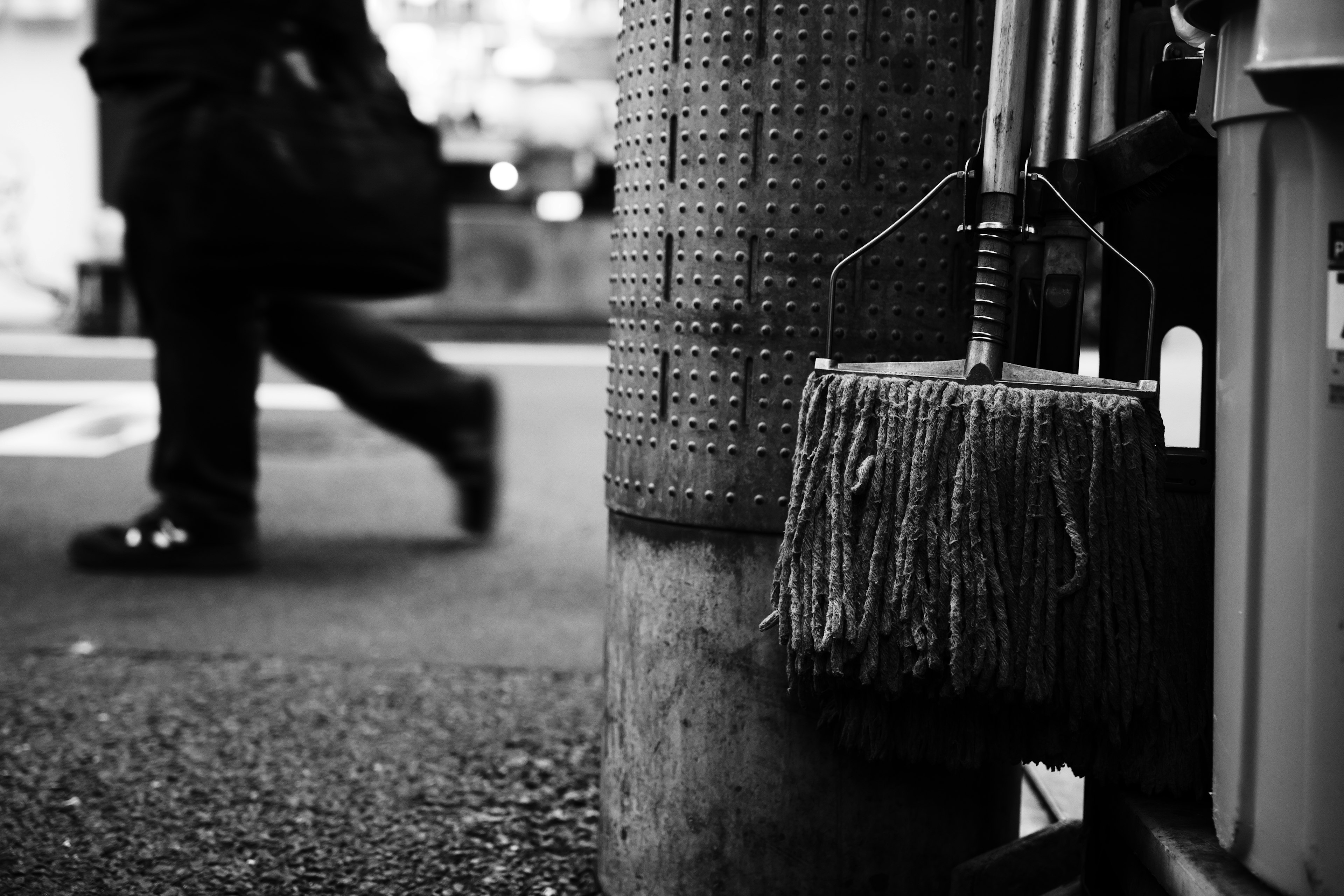 Imagen en blanco y negro de un trapeador colgado de un poste con un transeúnte