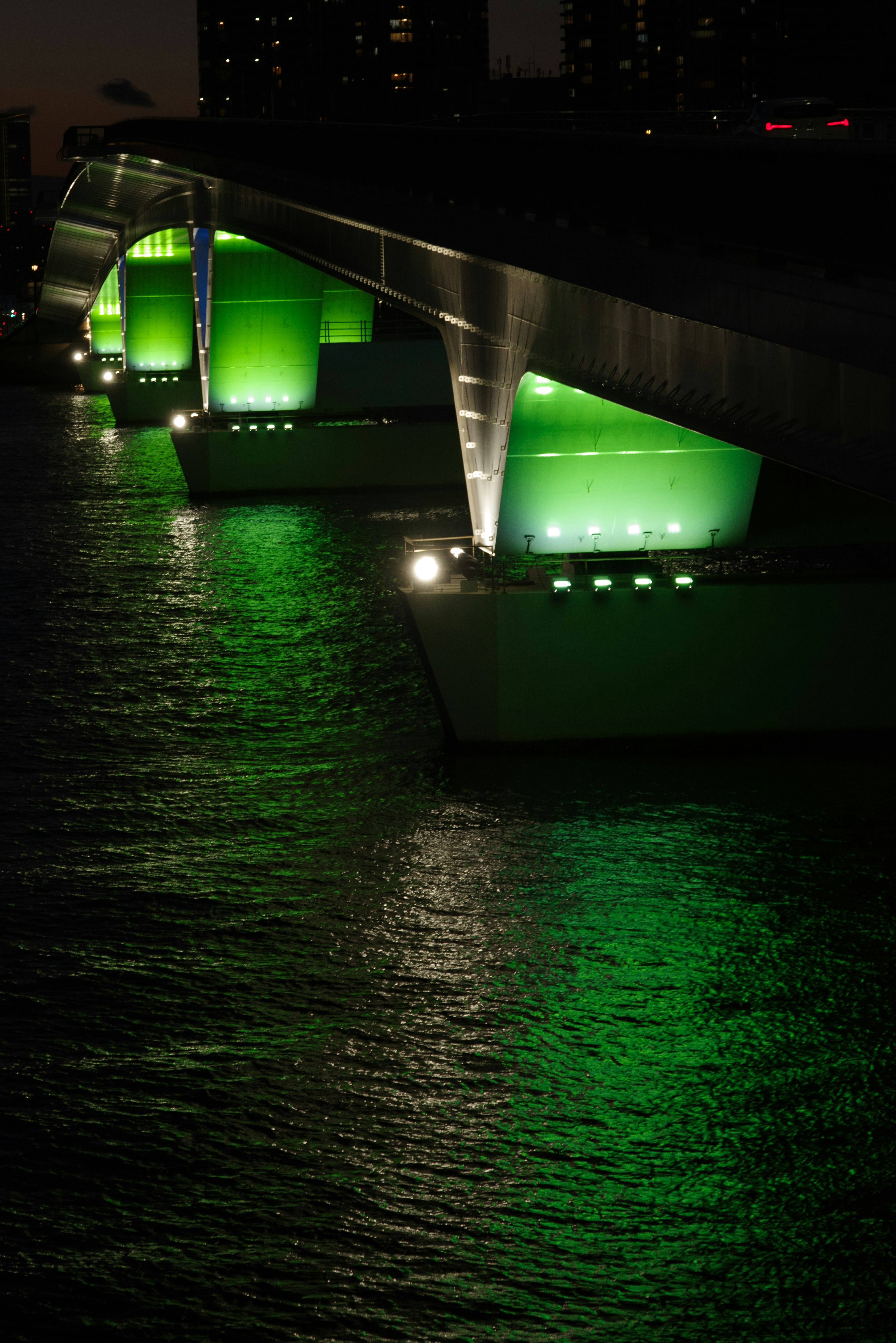 Pilares de puente iluminados en verde sobre un río por la noche