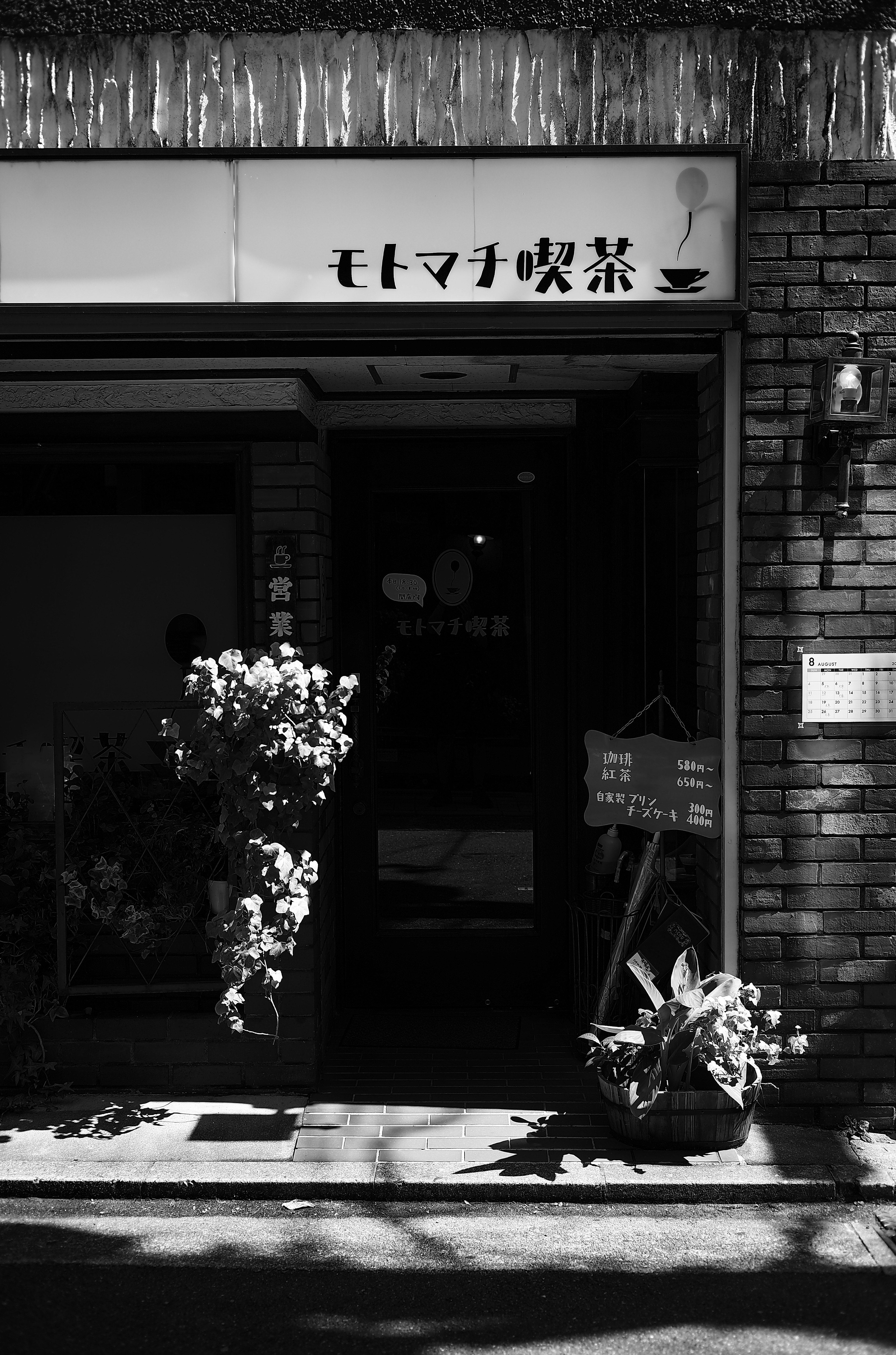 Black and white café entrance featuring plants and a sign