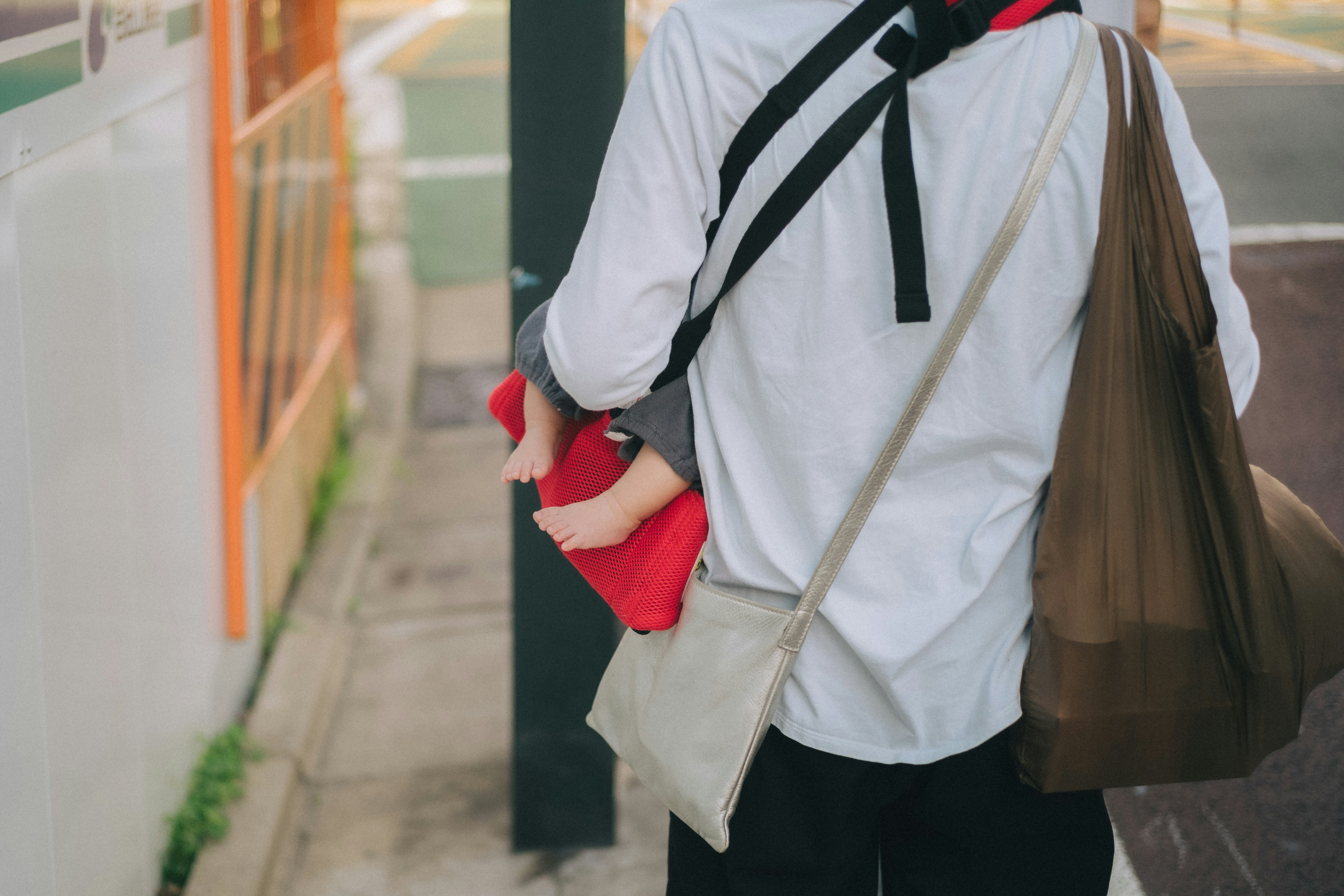 Person walking from behind carrying a red item and wearing a white shirt