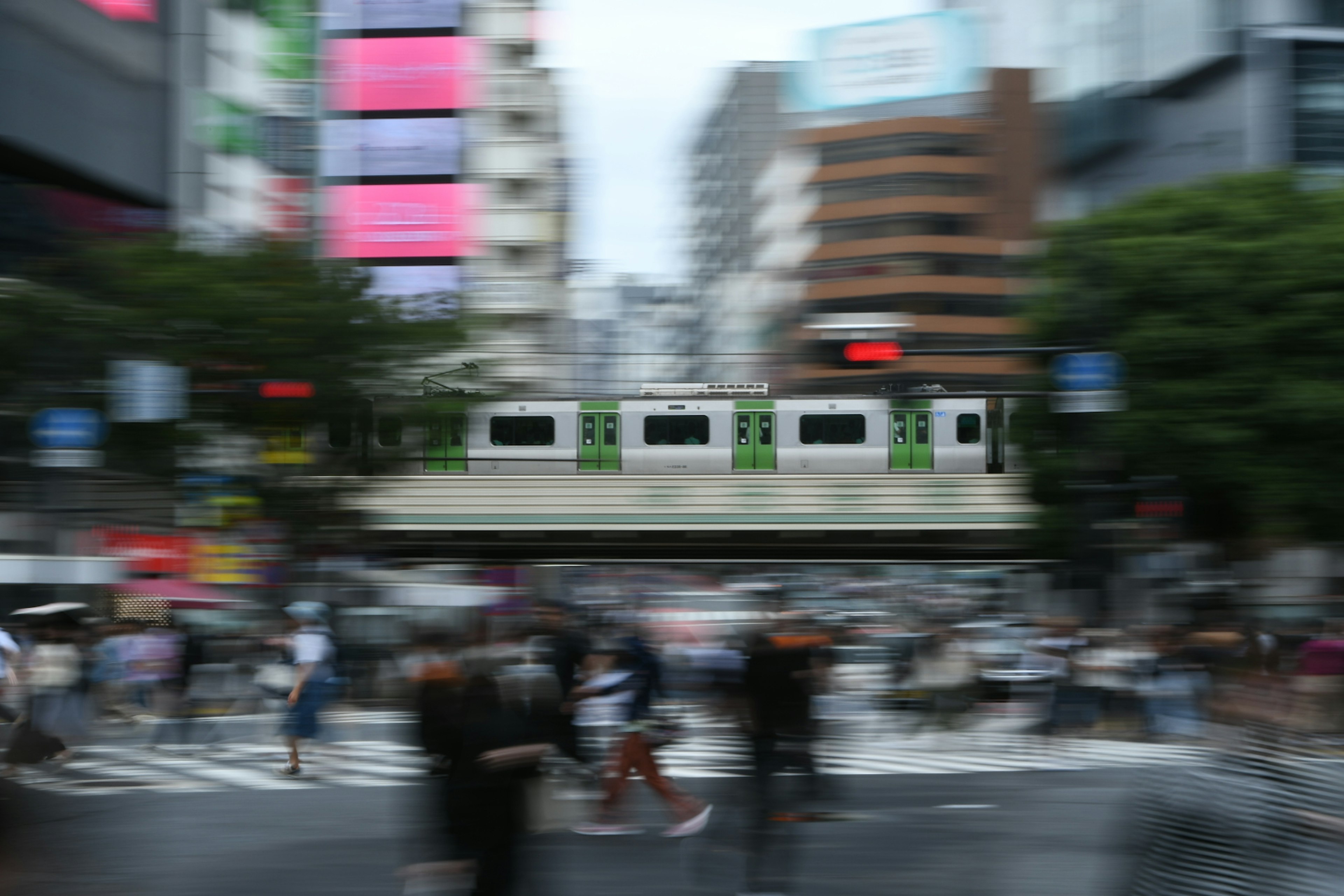 Blurred city intersection scene with people crossing and a train in the background