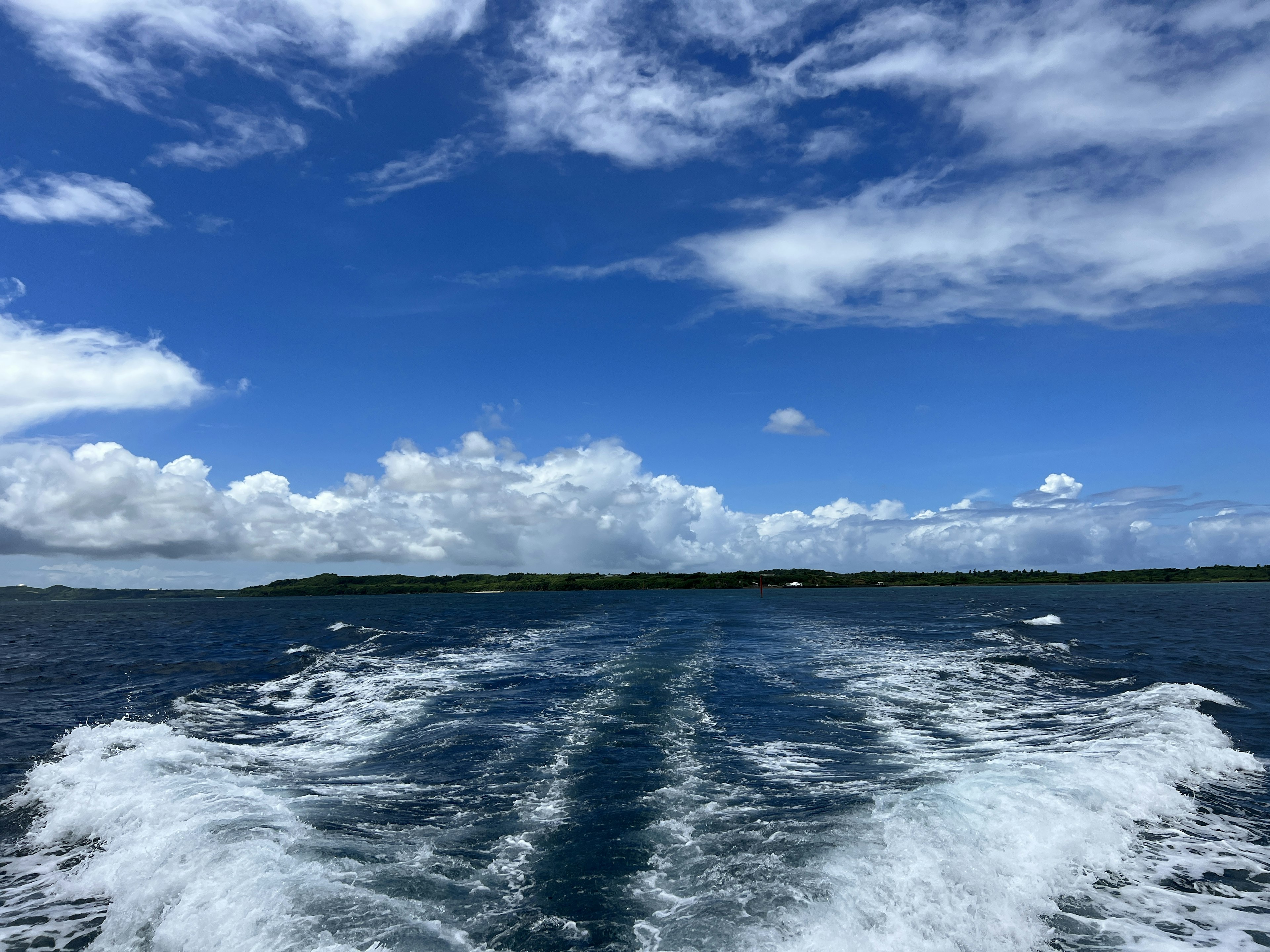 Pemandangan laut dengan langit biru dan awan putih serta jejak kapal di belakang