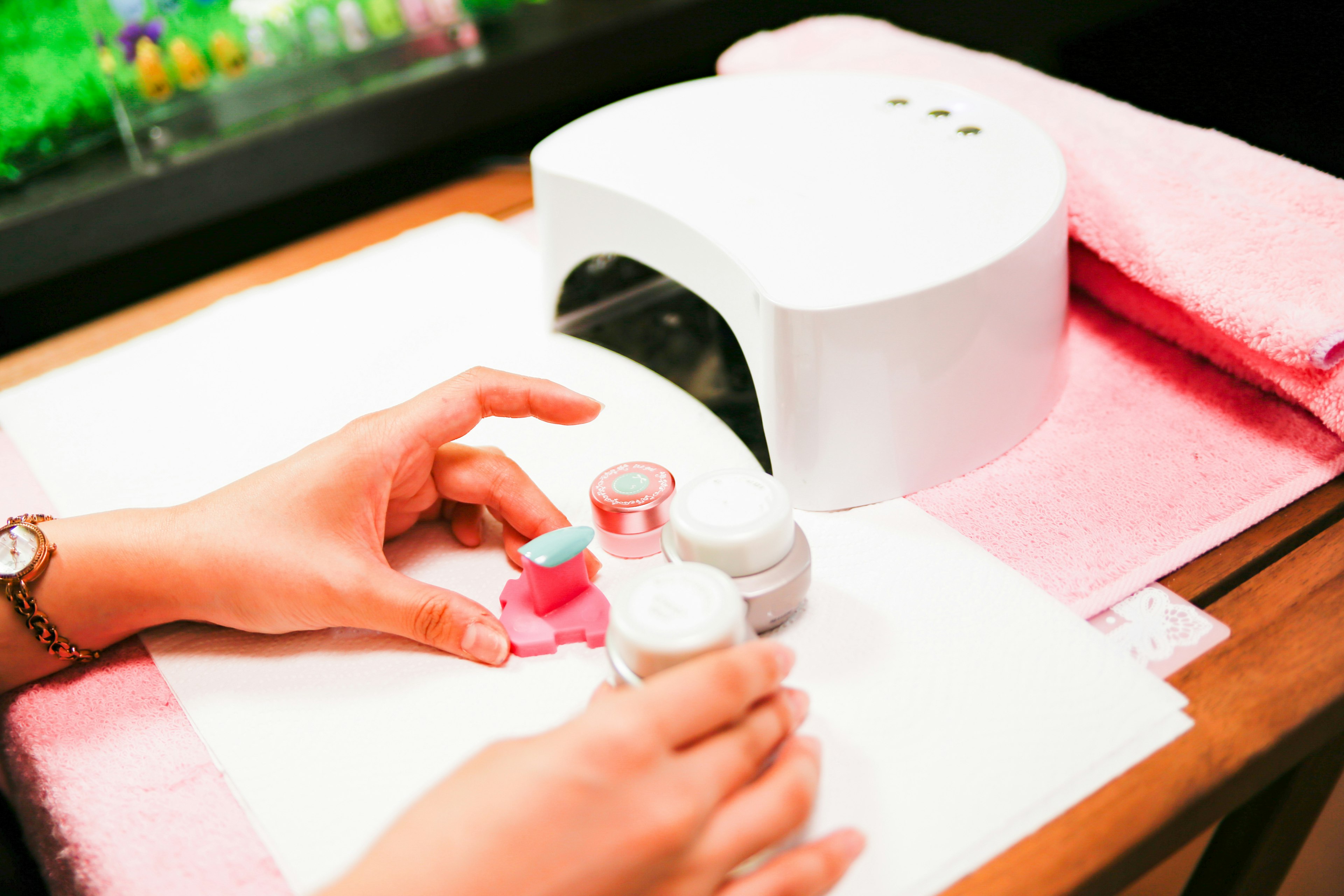 Hands applying nail polish with a UV lamp in a nail salon