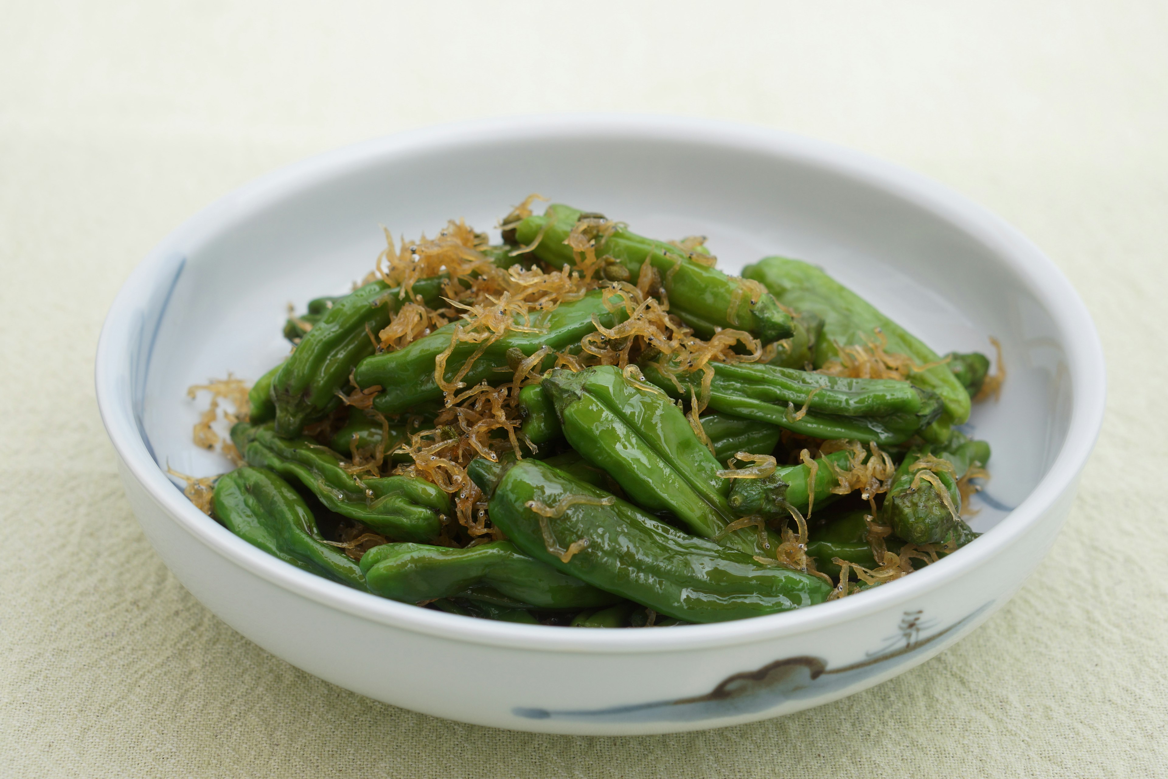 A bowl of sautéed shishito peppers topped with dried fish flakes