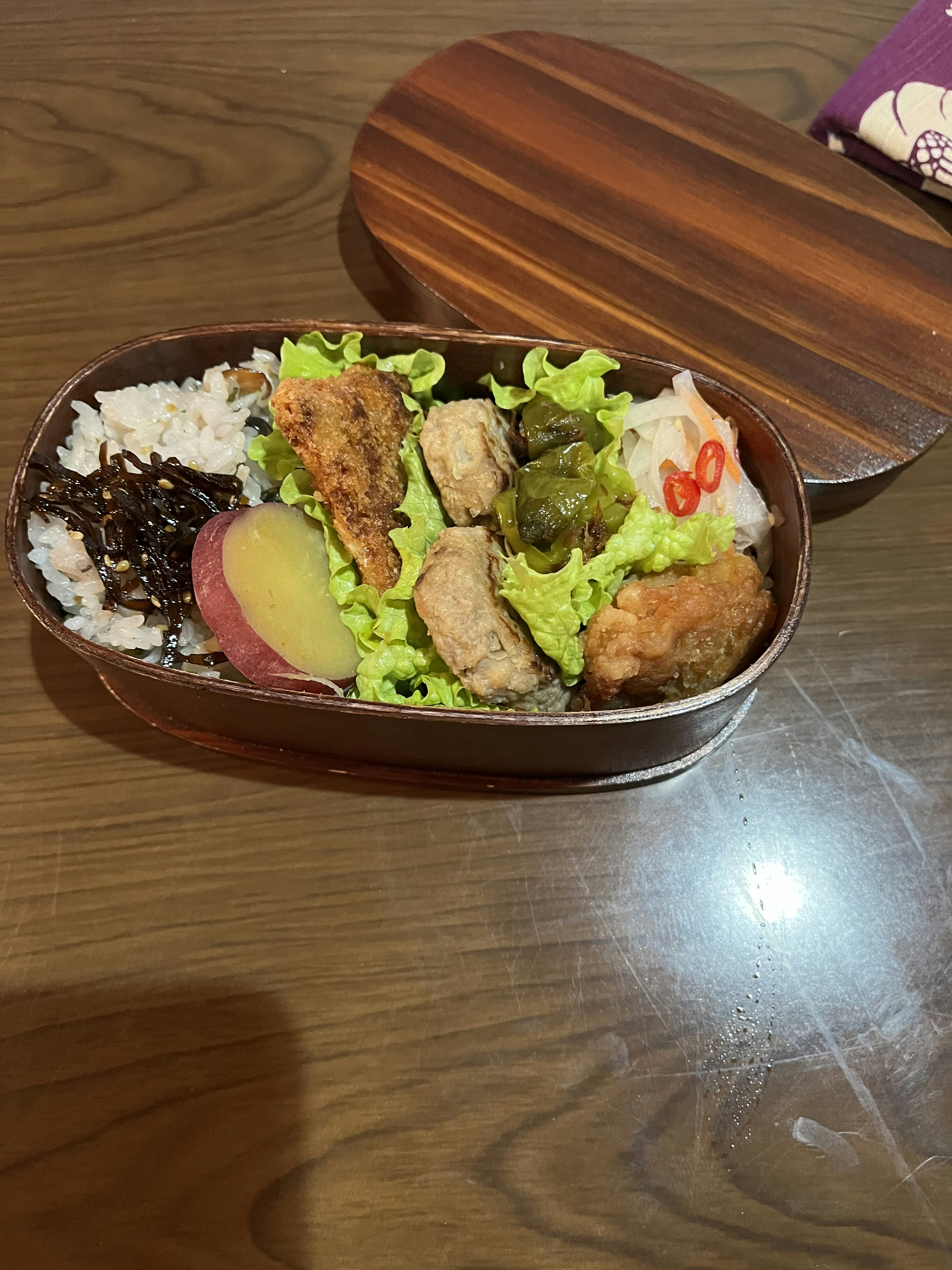 Bento box containing rice, fried chicken, lettuce, sweet potato, red chili, and seaweed