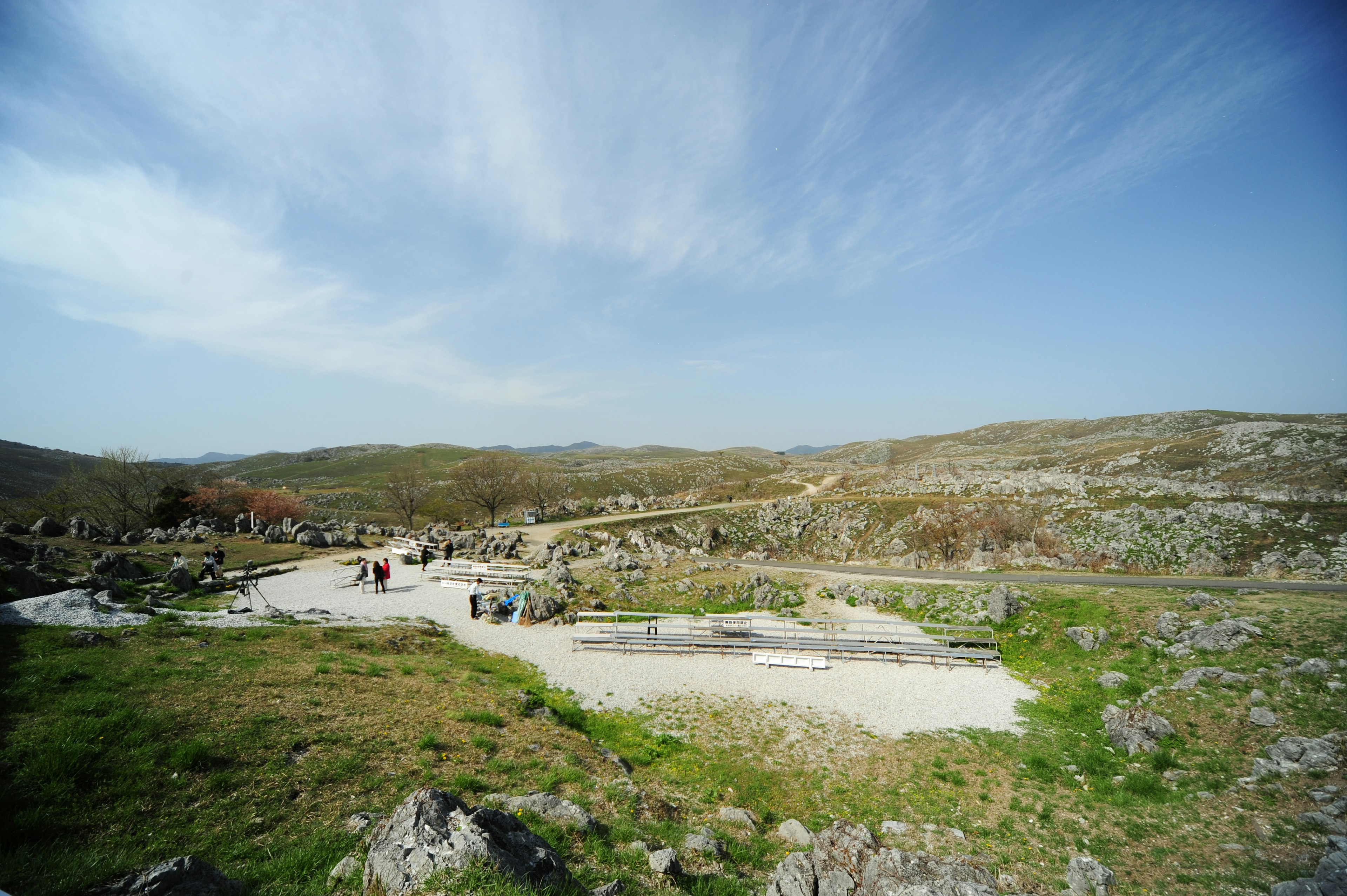 Vue panoramique d'un site archéologique entouré de verdure avec des visiteurs sous un ciel bleu