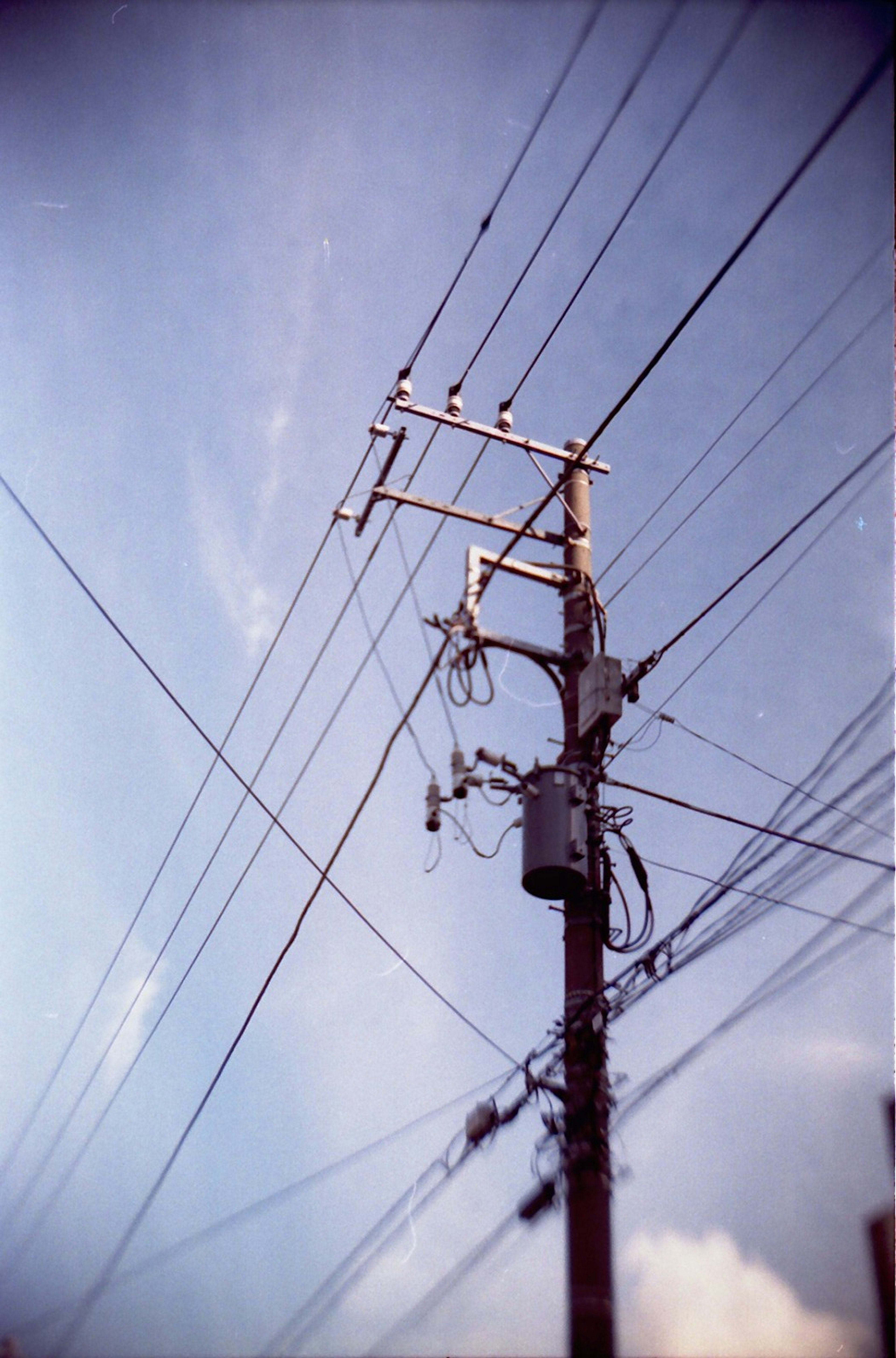 Strommast mit sich kreuzenden Stromleitungen vor blauem Himmel