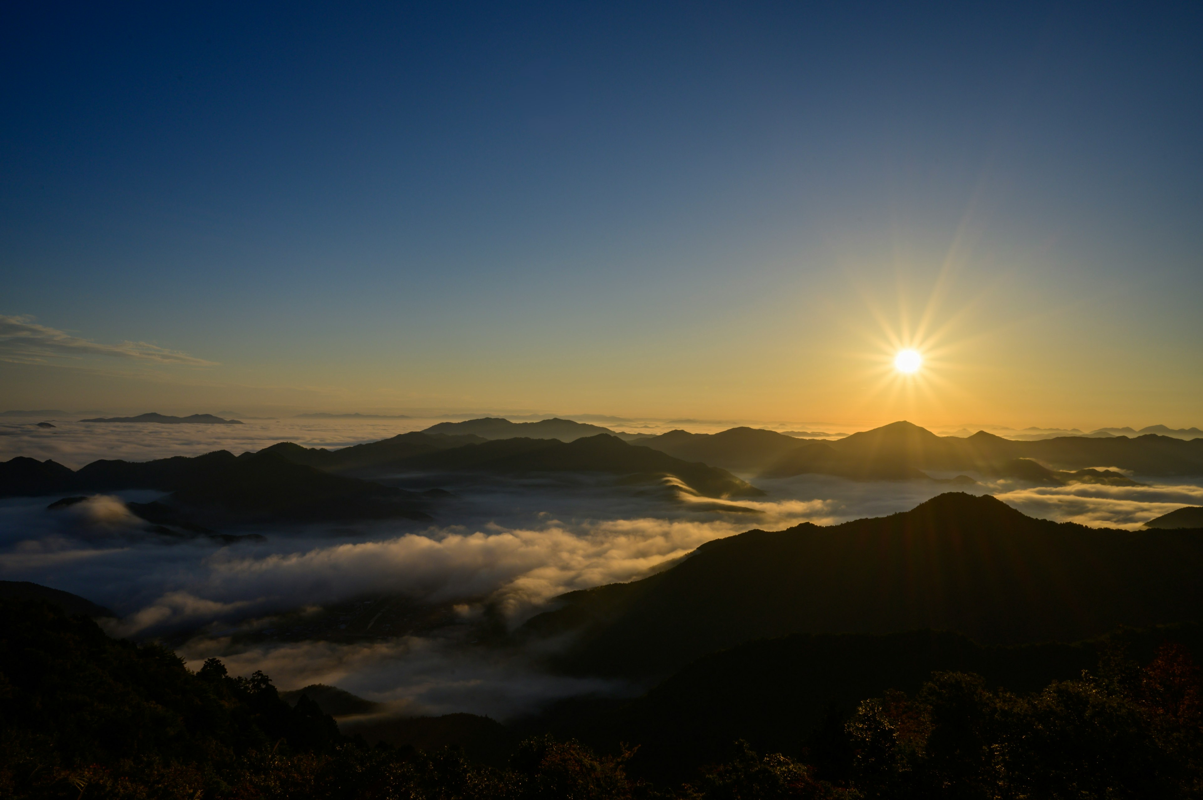 美麗的日出在山脈上方，霧氣瀰漫的山谷和晴朗的藍天