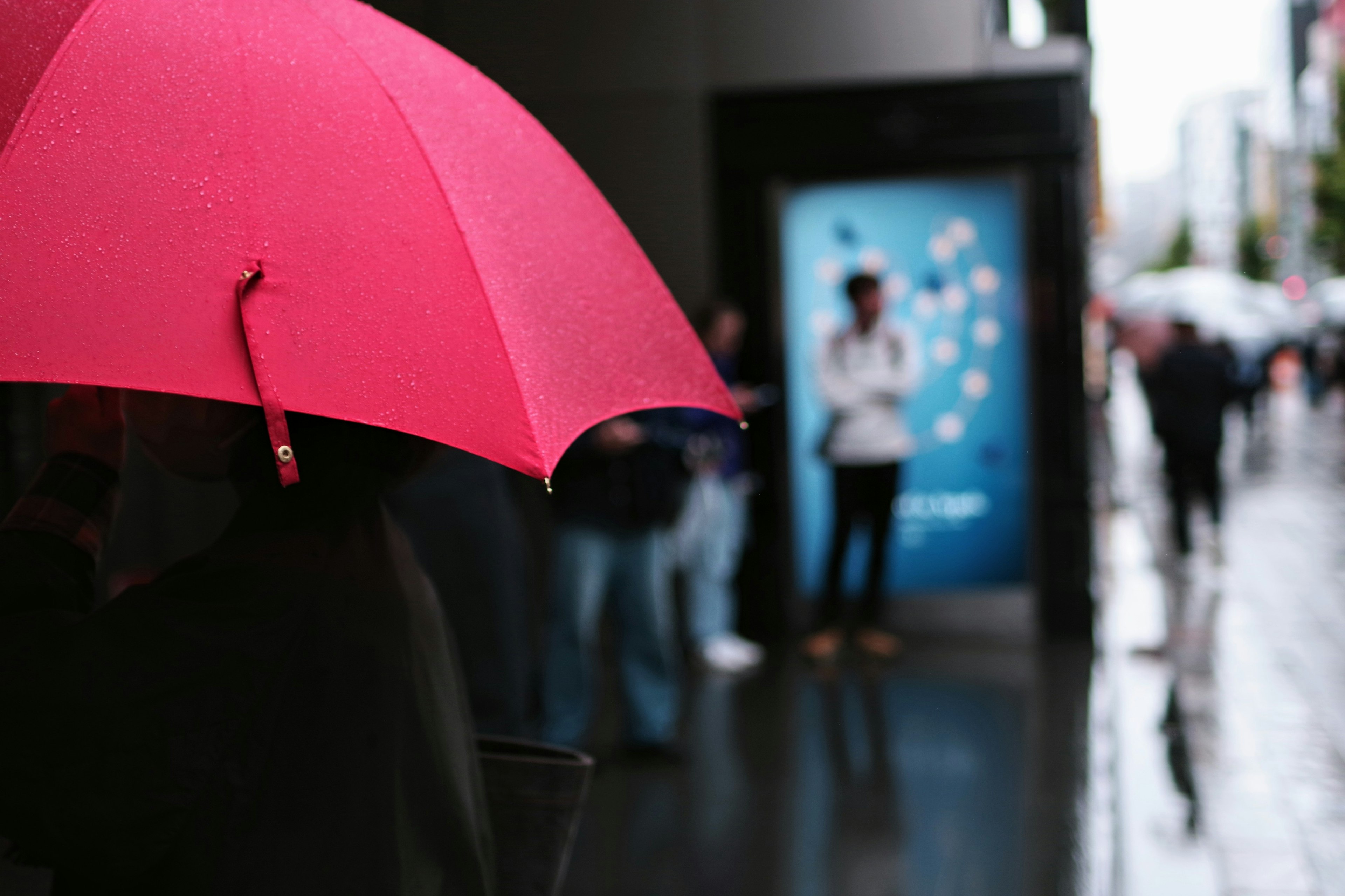 A person holding a pink umbrella in a rainy city scene