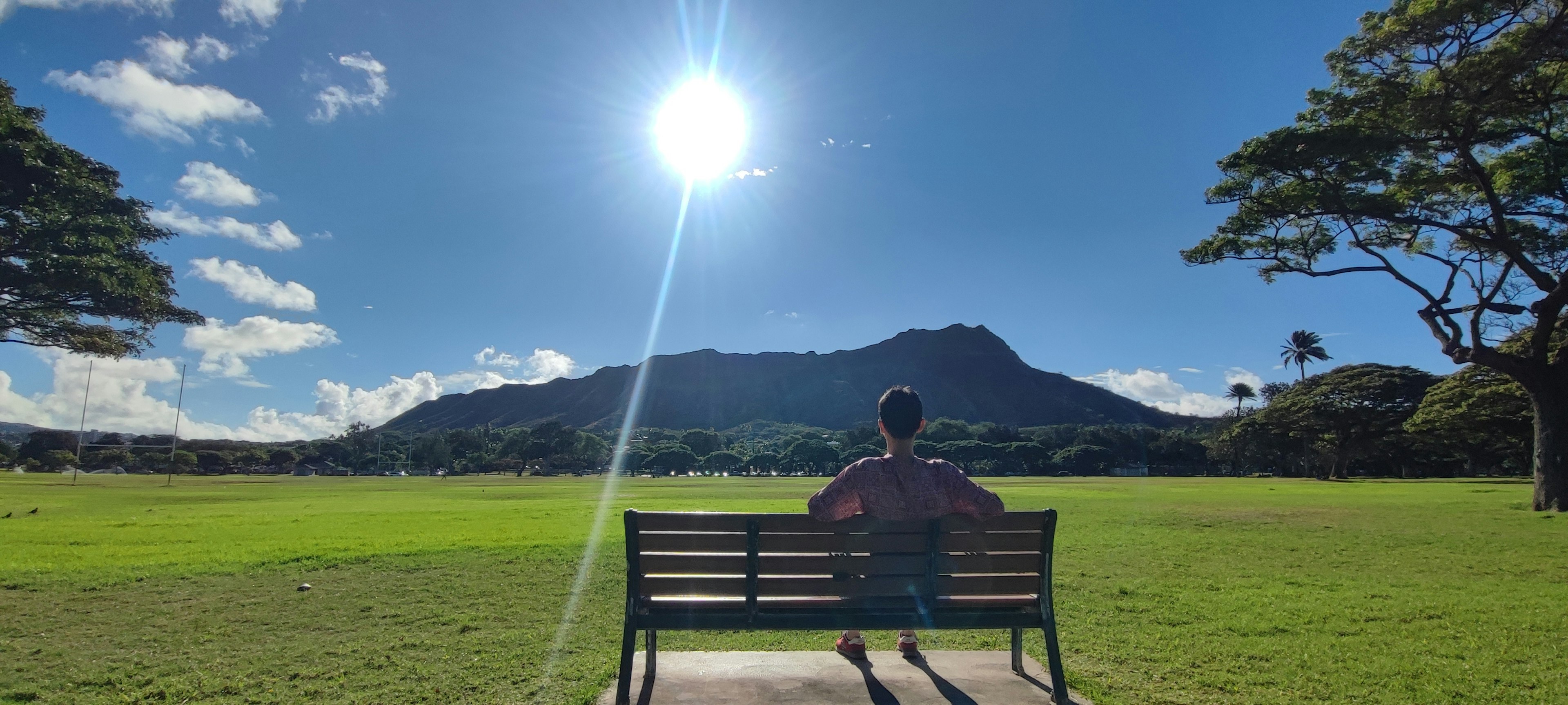 Silhouette d'une personne assise sur un banc avec une montagne en arrière-plan sous un ciel bleu clair