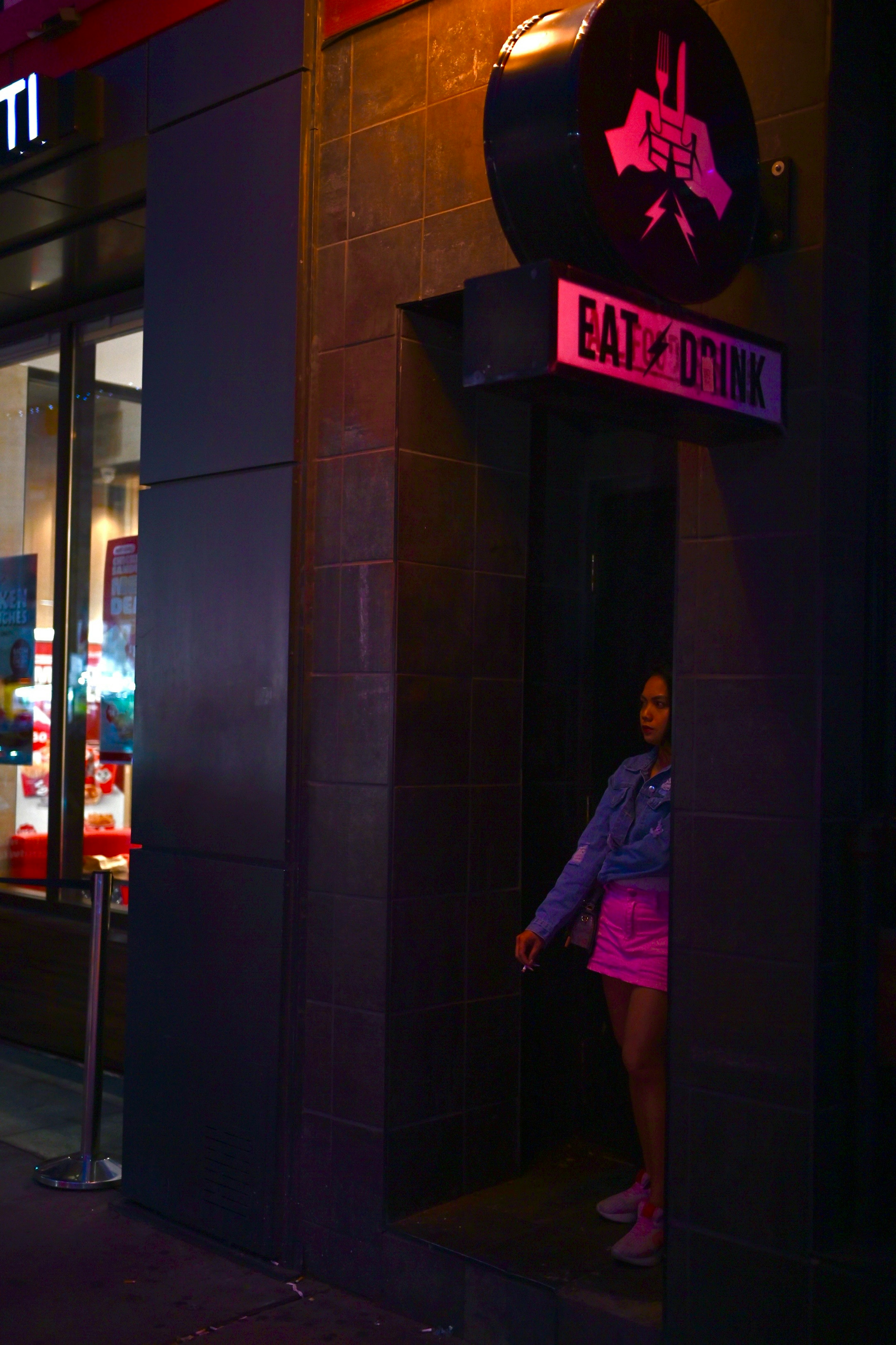 Una mujer de pie en una puerta con luz rosa en una calle oscura