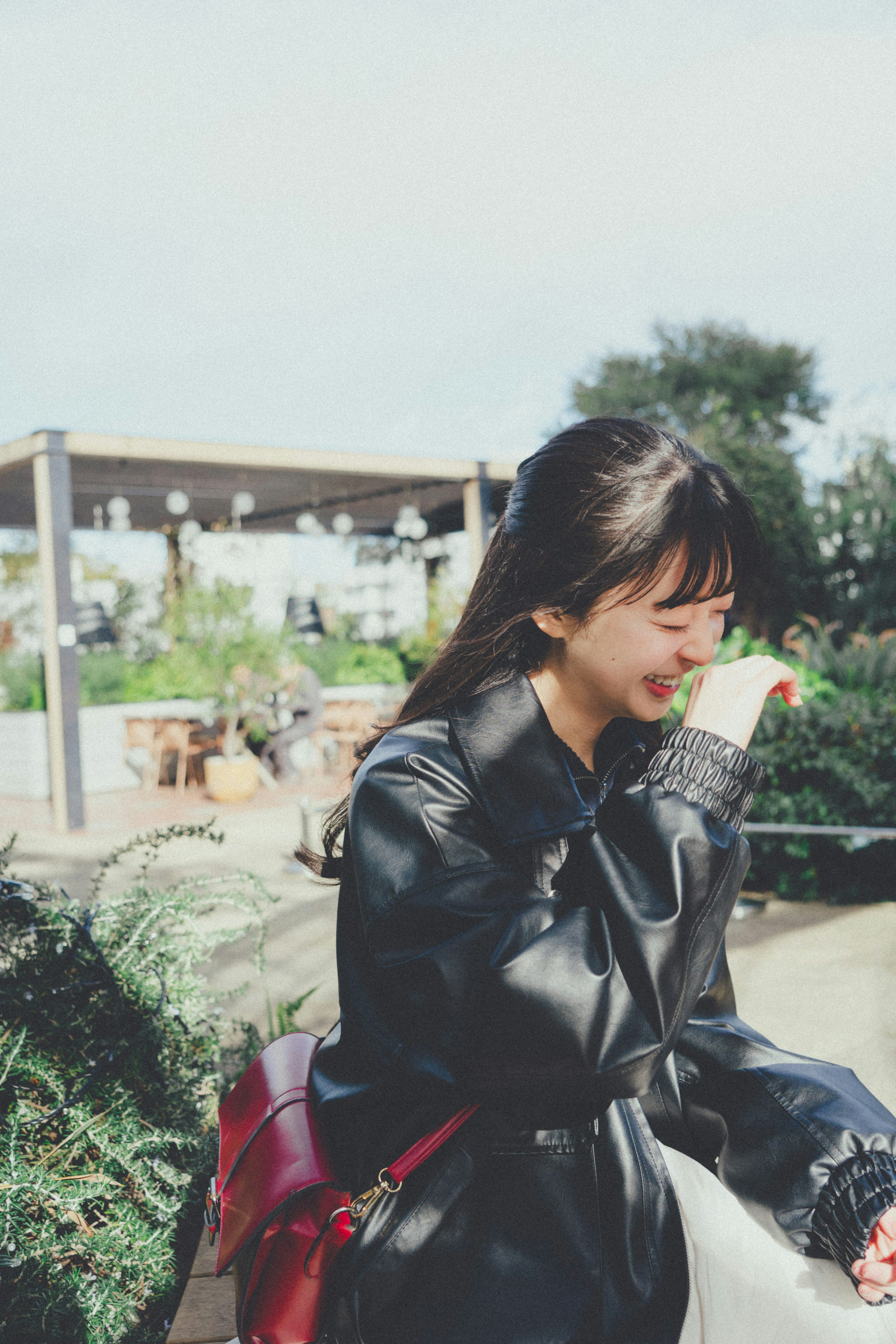 Jeune femme souriante en veste noire avec un sac rouge dans un jardin